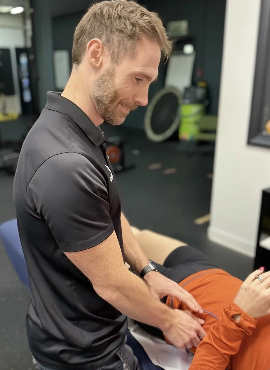A physical therapist performs an exercise to a patient in a gym. The therapist is focused and gently supports the patient's arm.