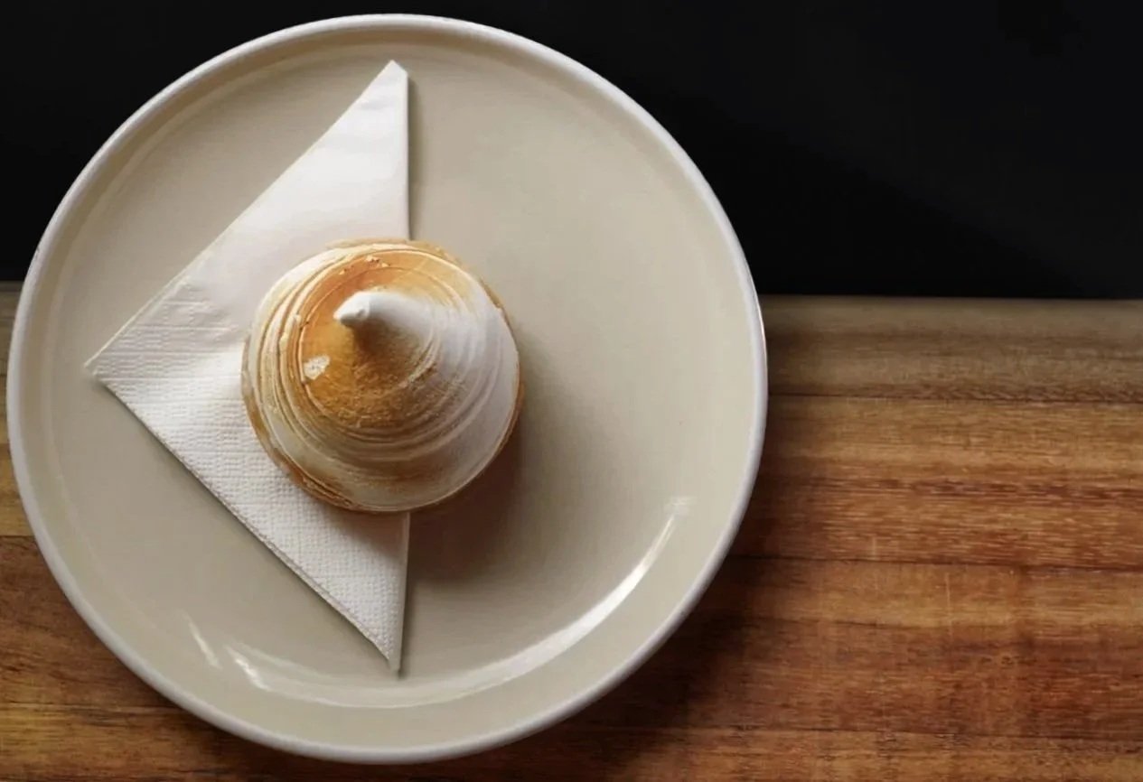 A seashell on a plate with a napkin, placed on a wooden surface.  Food Photo Co.