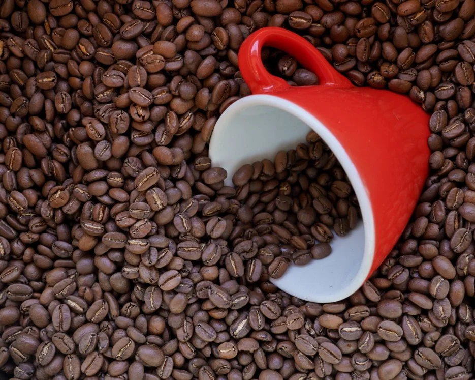 Red mug tipped over among roasted coffee beans.