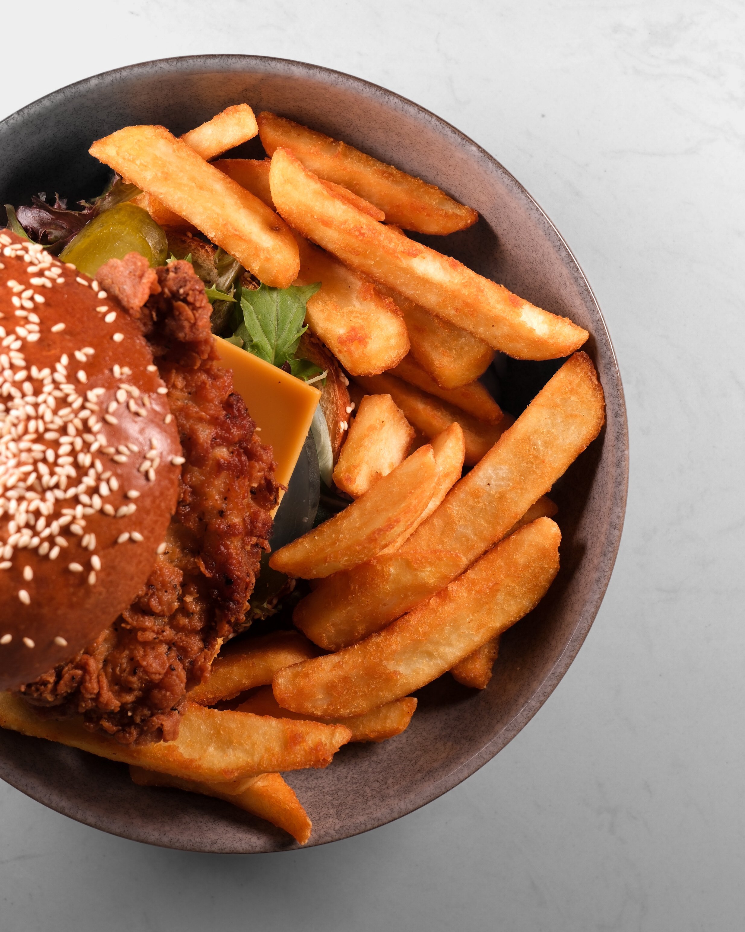 French fries, lettuce, pickles, cheese, and a burger with sesame seed bun in a bowl