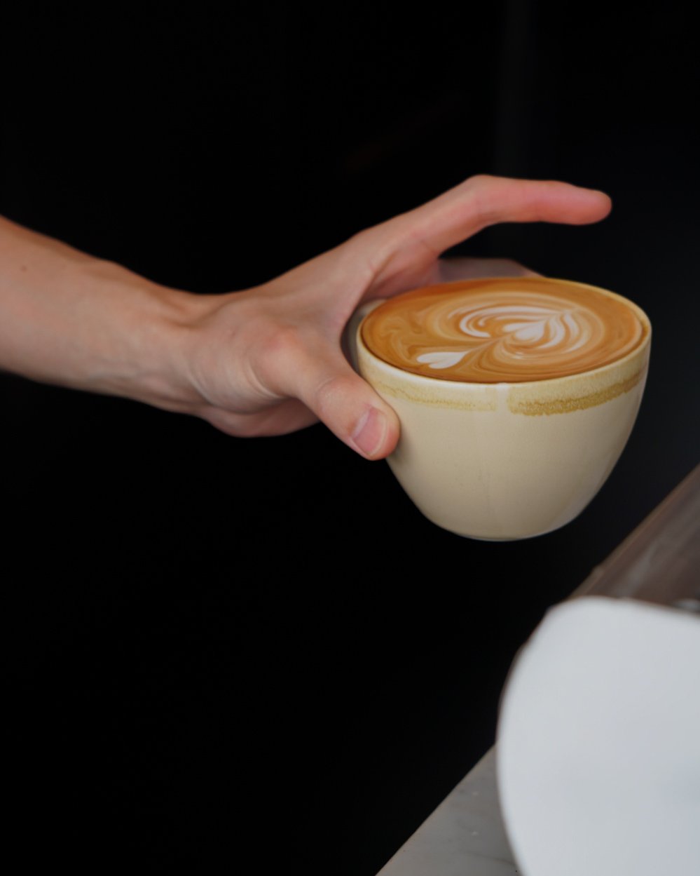 A person holding a ceramic cup of coffee with latte art on top.  Food Photo Co.