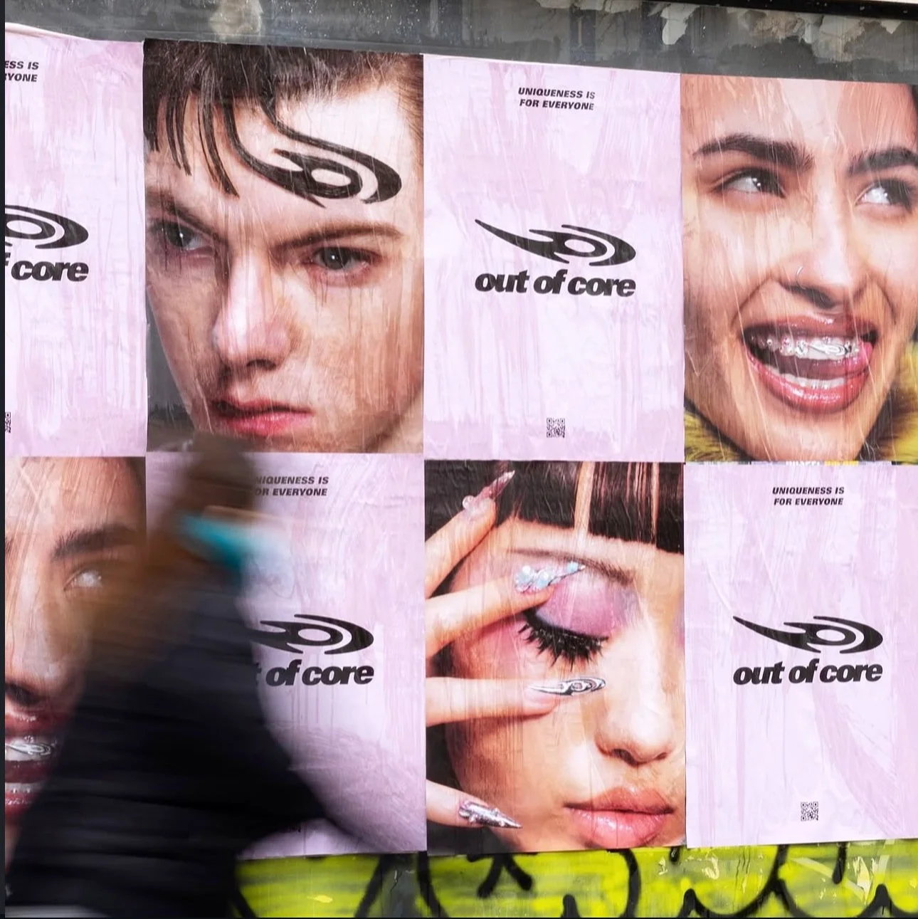 Una parete con poster pubblicitari di vario tipo, alcuni ritratti di persone, alcuni con trucco evidente e accessori come piercing, con il logo 'art of core' e la scritta 'UNIQUE IS FOR EVERYONE'.