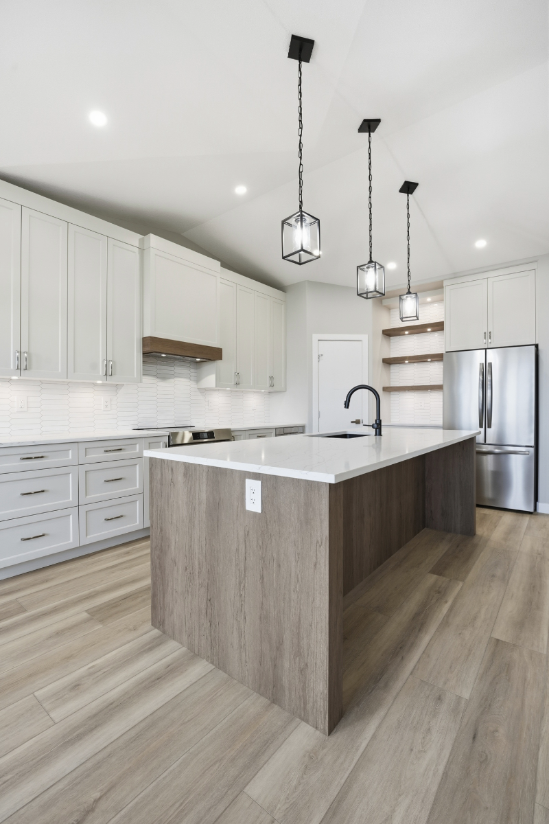 Modern kitchen with white cabinets, a large island with a white countertop, stainless steel refrigerator, black faucet, and hanging pendant lights.
