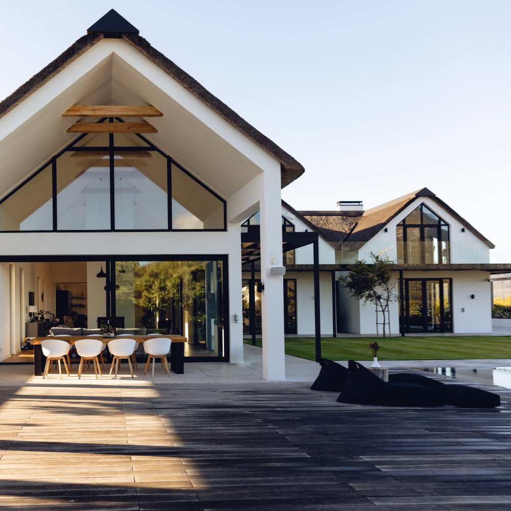 Modern house with large glass windows, white walls, and a wooden deck area.