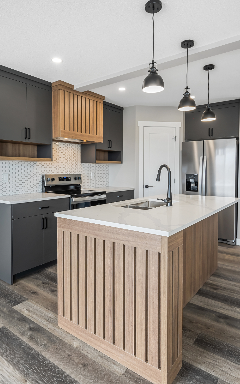 Modern kitchen with grey and wood cabinets, white countertop island, stainless steel appliances, pendant lighting, and hexagonal tile backsplash.