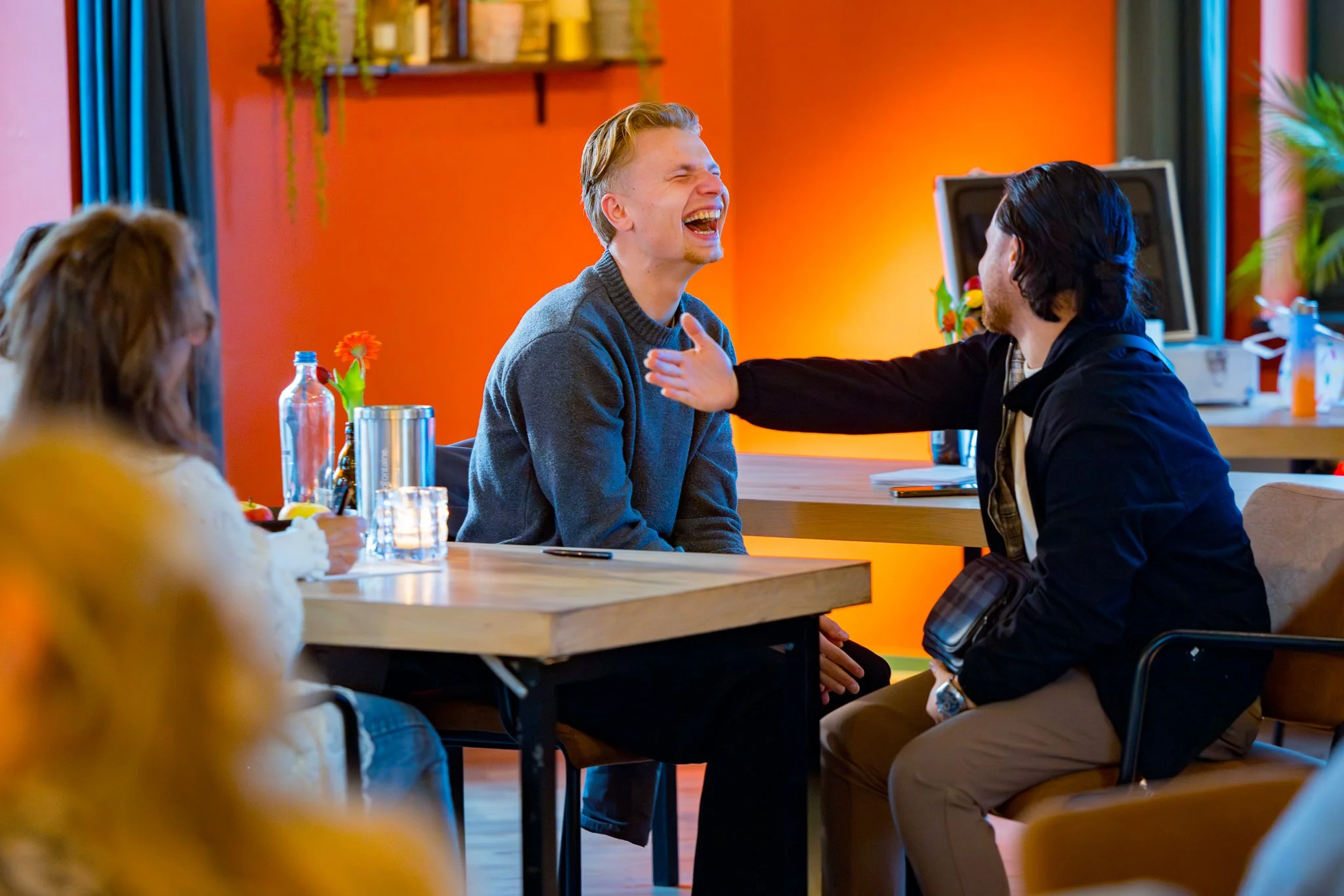 Mensen lachen en praten samen in een gezellige, kleurrijke ruimte met oranje muren.
