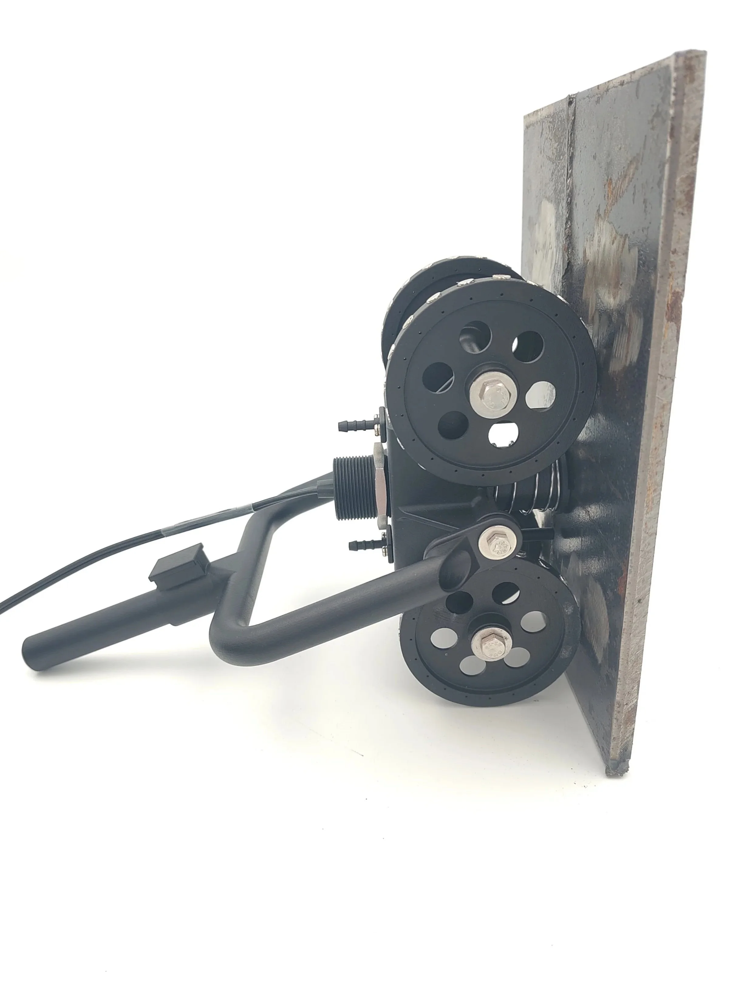 A mechanical device with two black pulleys, a metal base, and connected black tubes or wires, mounted on a flat surface.