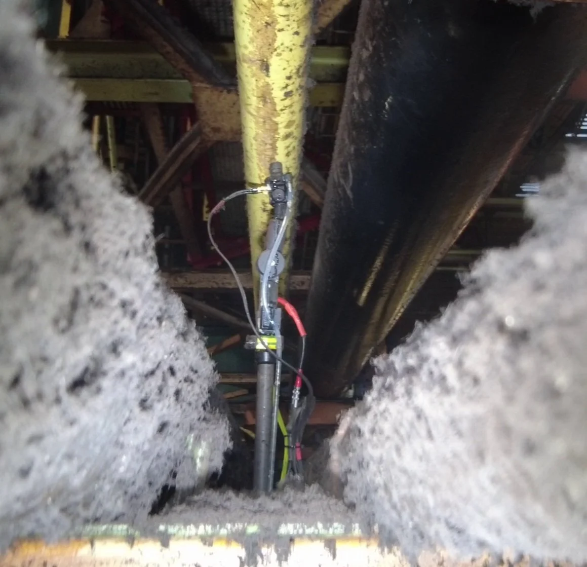 View of industrial machinery and piping in a construction or maintenance setting, seen from ground level among insulation or insulation material.