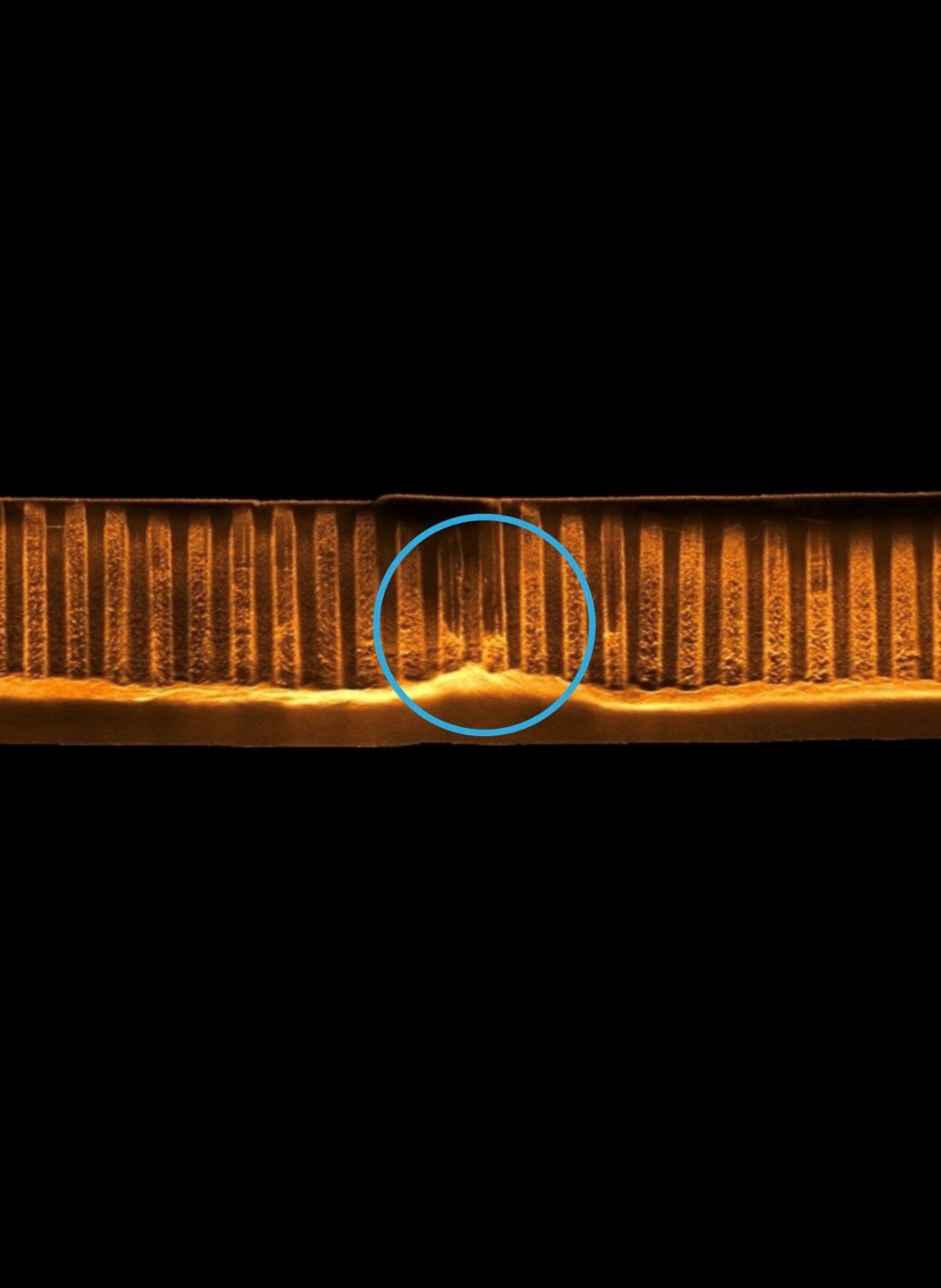Close-up of a metallic object with vertical ridges, illuminated with warm light, and a blue circle highlighting a specific section.