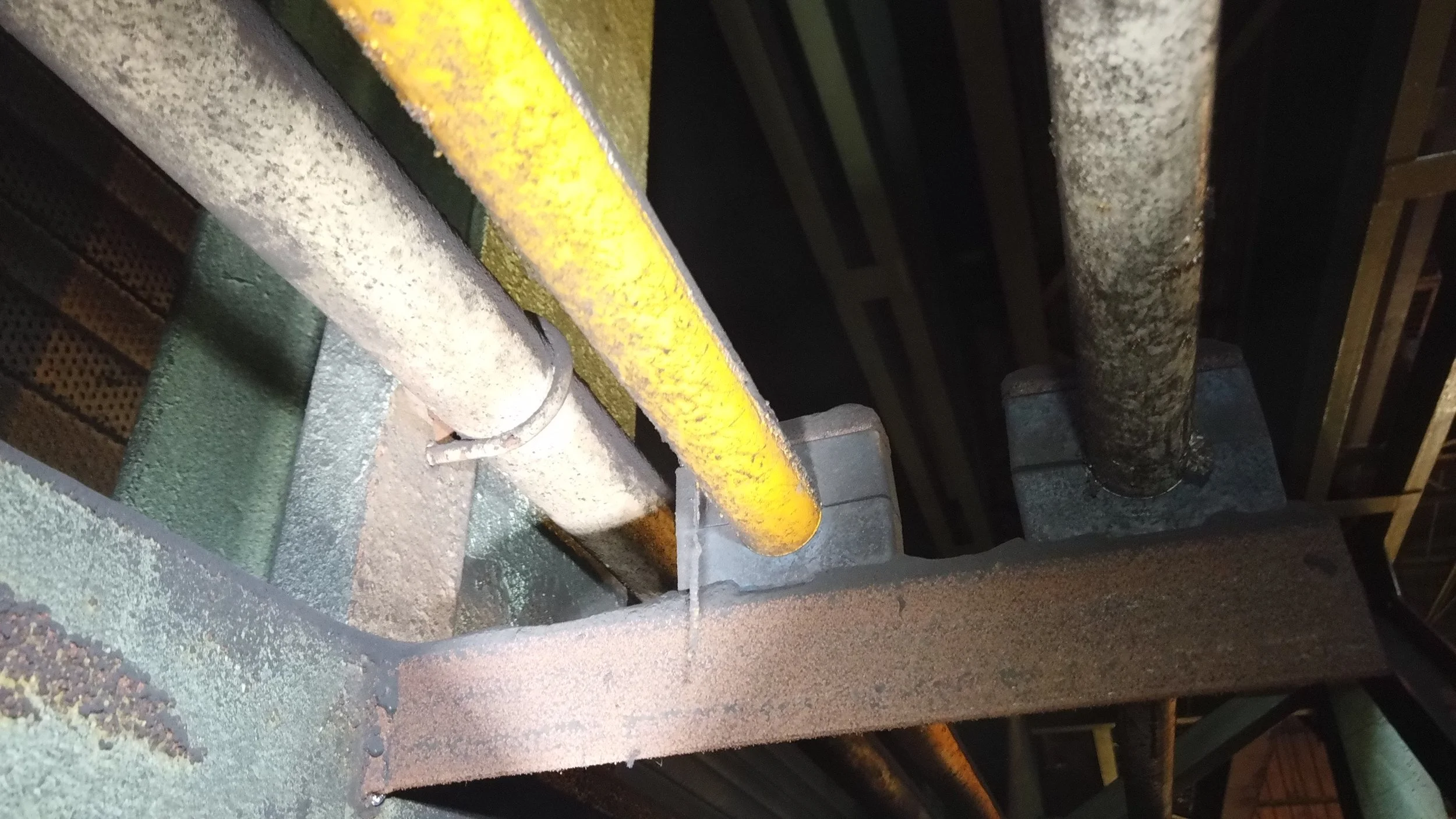Close-up view of oil pipes and support structures on machinery, showing rust and dirt accumulation.