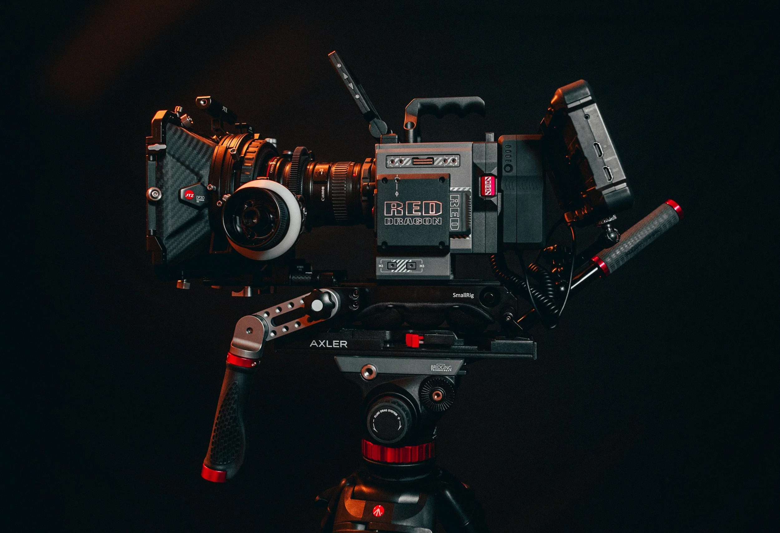 Professional cinema camera mounted on a tripod with various accessories, against a dark background.