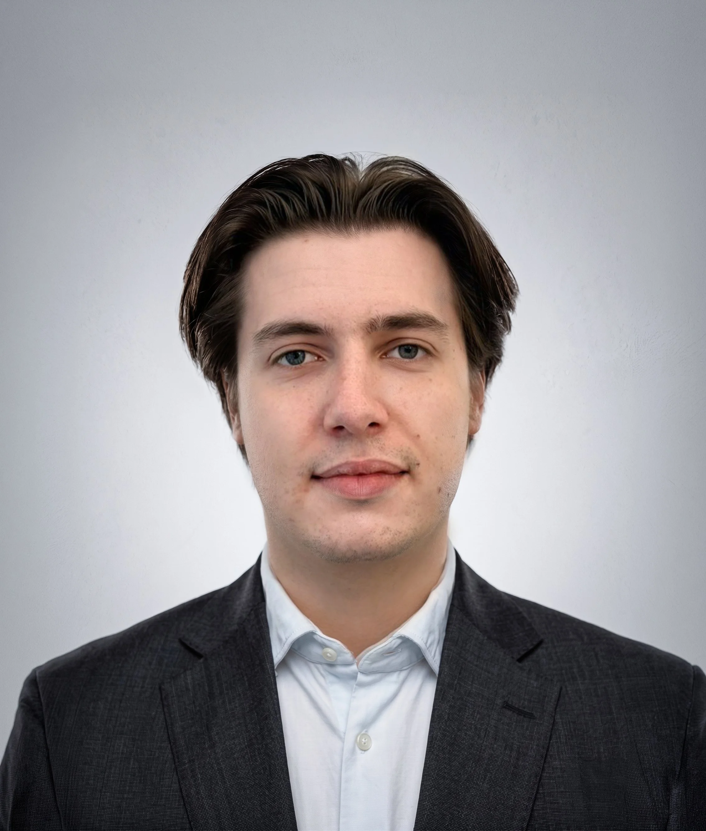 Portrait of a man with short, brown hair, blue eyes, wearing a navy blazer and a light blue dress shirt against a plain, light gray background.