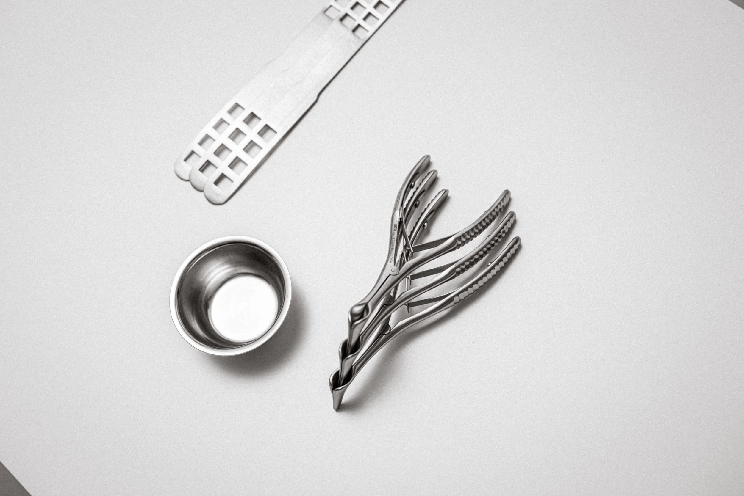 Stahlklemmen, ein Metallbecher und medizinische oder chirurgische Instrumentscheren auf einer weißen Oberfläche.