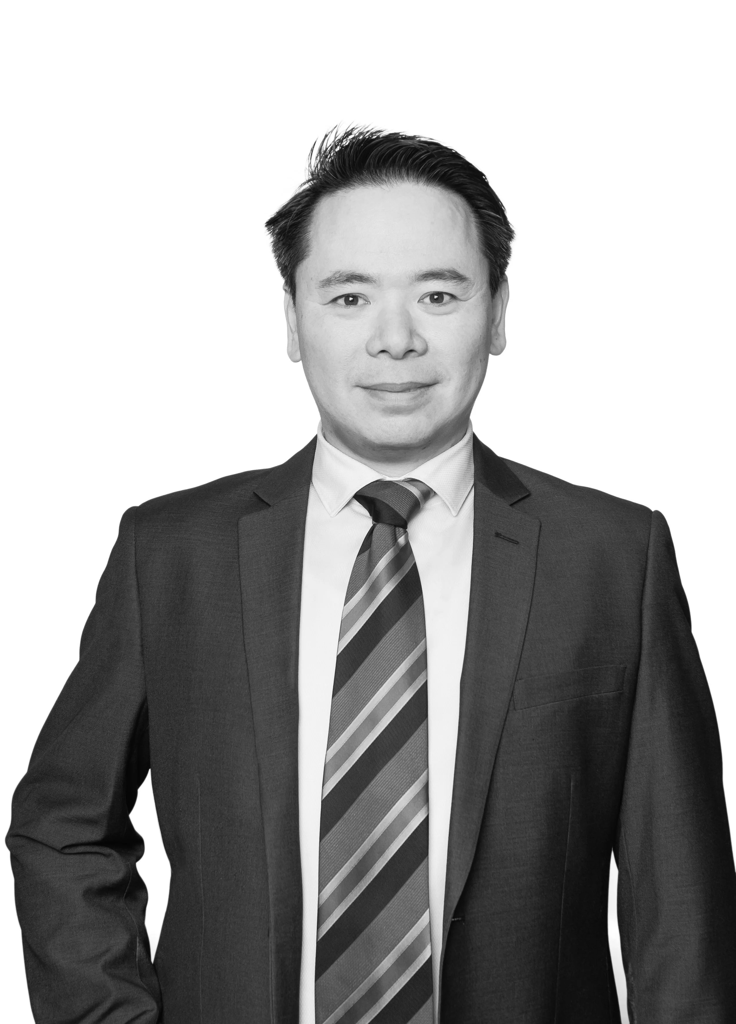 Black and white portrait of a man in a business suit, white shirt, and striped tie, smiling with one hand on his hip, against a white background.
