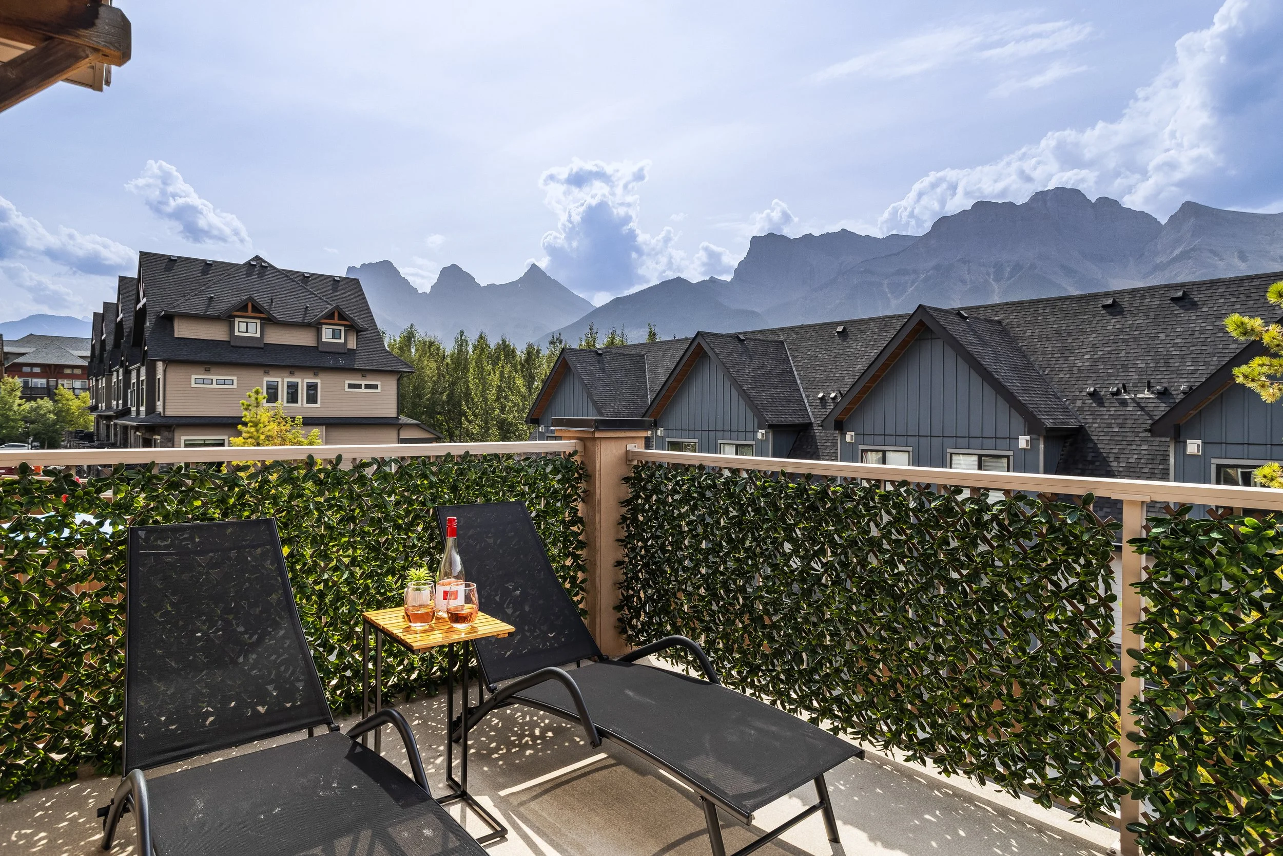 Multiple modern houses with blue and gray exteriors and steep roofs, set against a backdrop of snow-capped mountains and a clear blue sky.