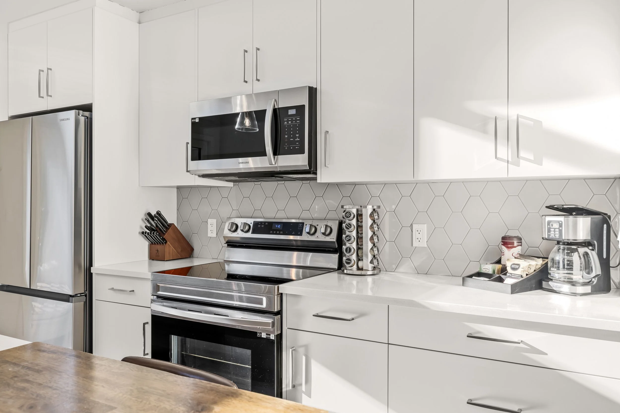 Modern kitchen with white cabinets, stainless steel appliances, a wooden dining table, and bar stools near a large sliding glass door leading to a balcony outdoor area.