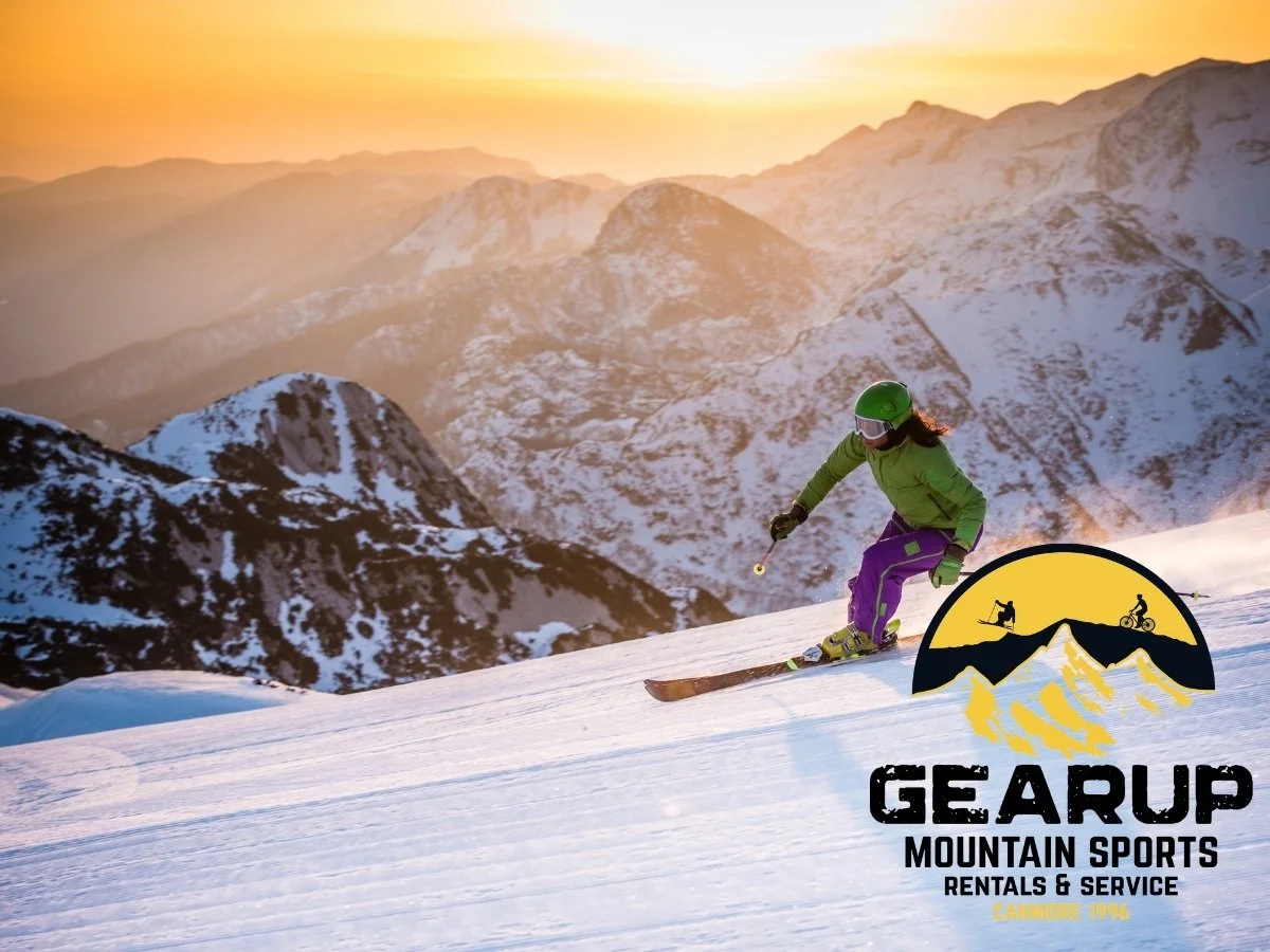A person skiing down a snow-covered mountain during sunset, with snow-capped mountains in the background and a Gearup Mountain Sports Rentals & Service logo in the bottom right corner.