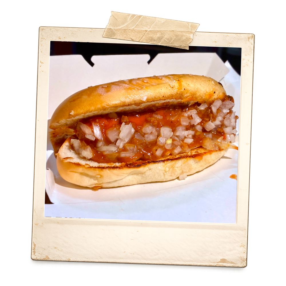 A hot dog with chopped onions in a bun, served inside a white box.