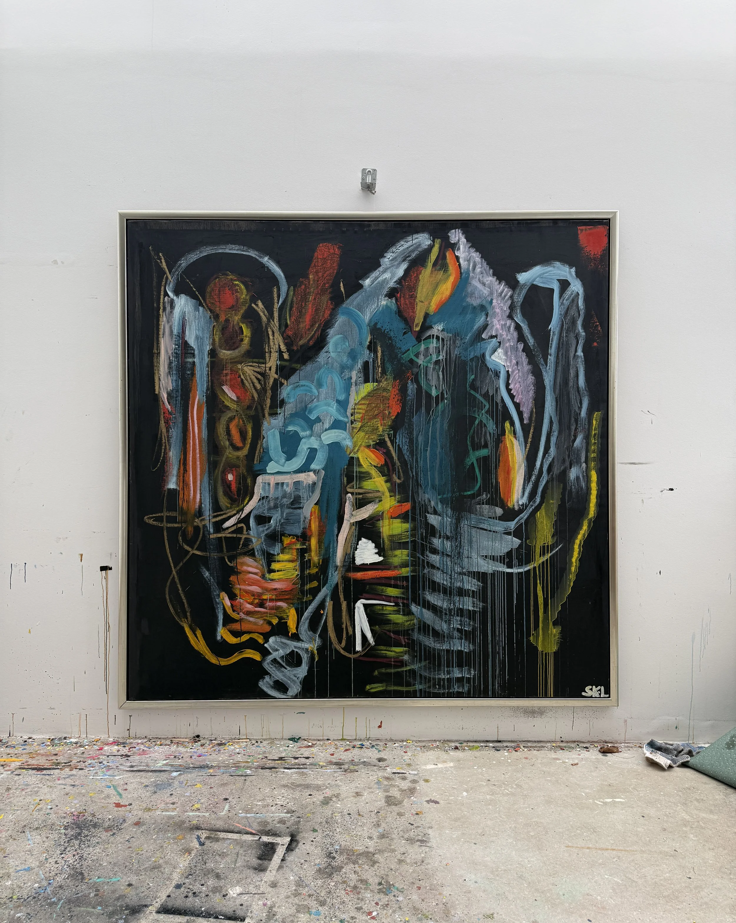 Abstract colorful painting with blue, red, yellow, and black strokes on a black background, signed 'SKL' in the bottom right corner, hung on a white wall in an art studio I Svend Kindt-Larsen I Abstract Artist I Copenhagen, Denmark