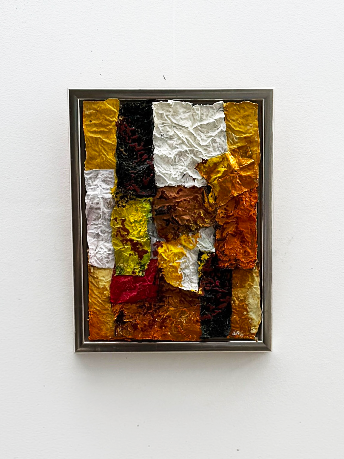 Abstract mixed media artwork with crumpled textured paper in various colors including white, yellow, red, black, brown, and orange, framed and mounted on a white wall I Svend Kindt-Larsen I Abstract Artist I Copenhagen, Denmark 