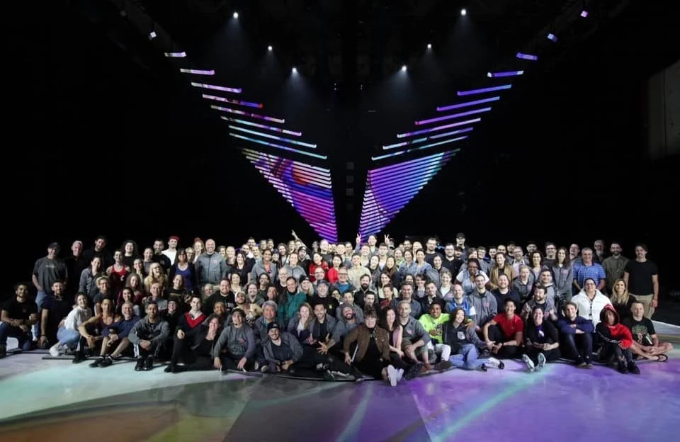 A large group of people posing together on a stage with colorful light displays above them.