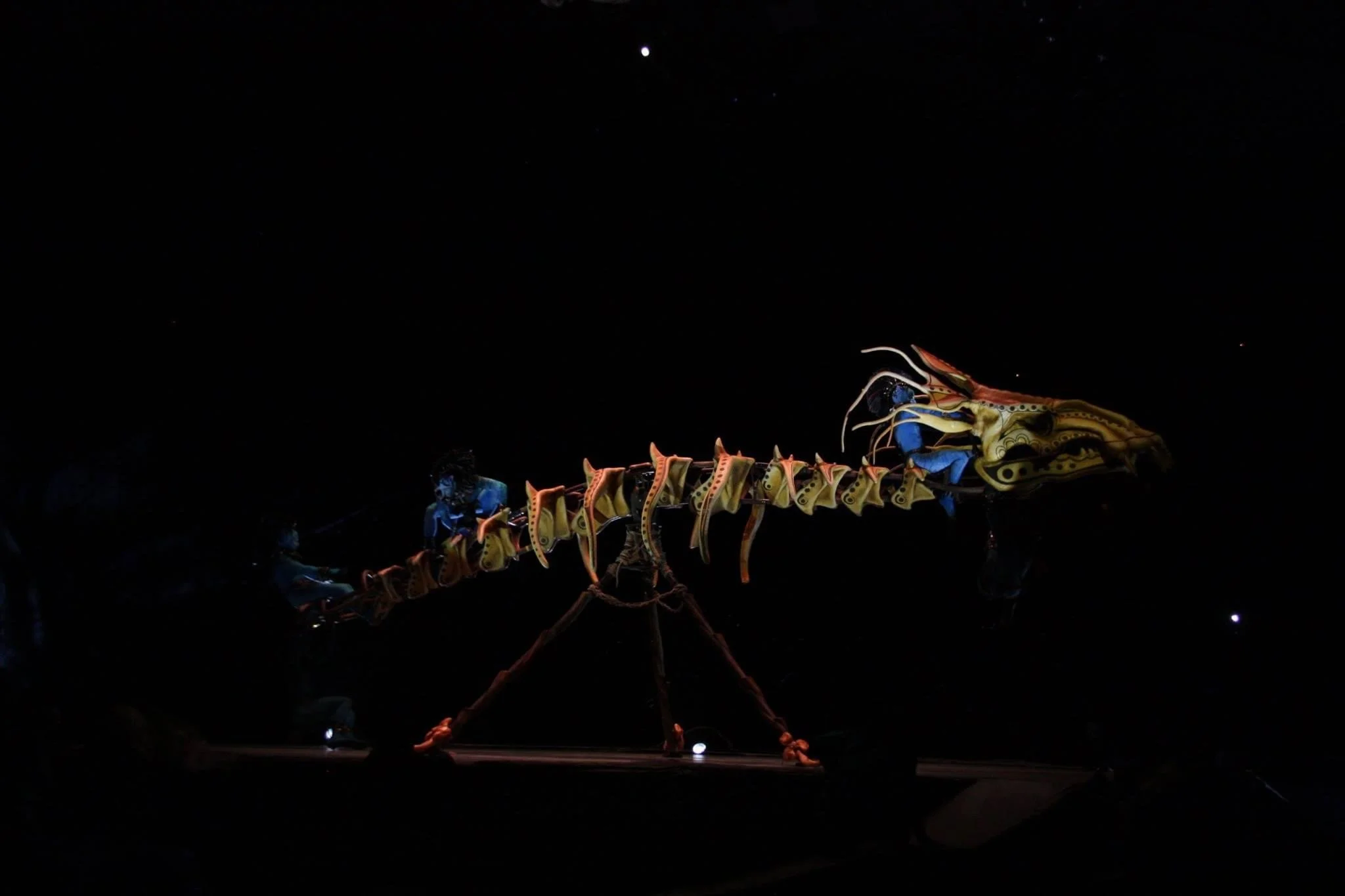 A dark stage featuring a large, acrobatic apparatus operated by performers, with projected stars visible on the set backdrop.