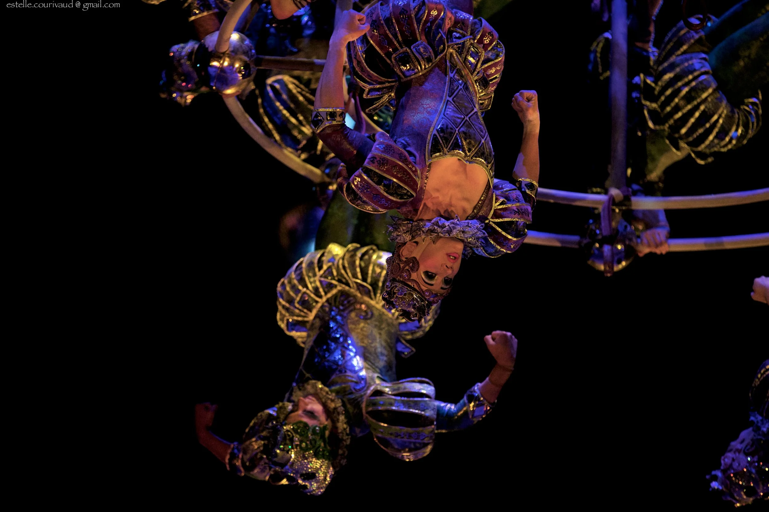 The House of Dancing Water performers in colorful costumes performing acrobatics on stage with black background.