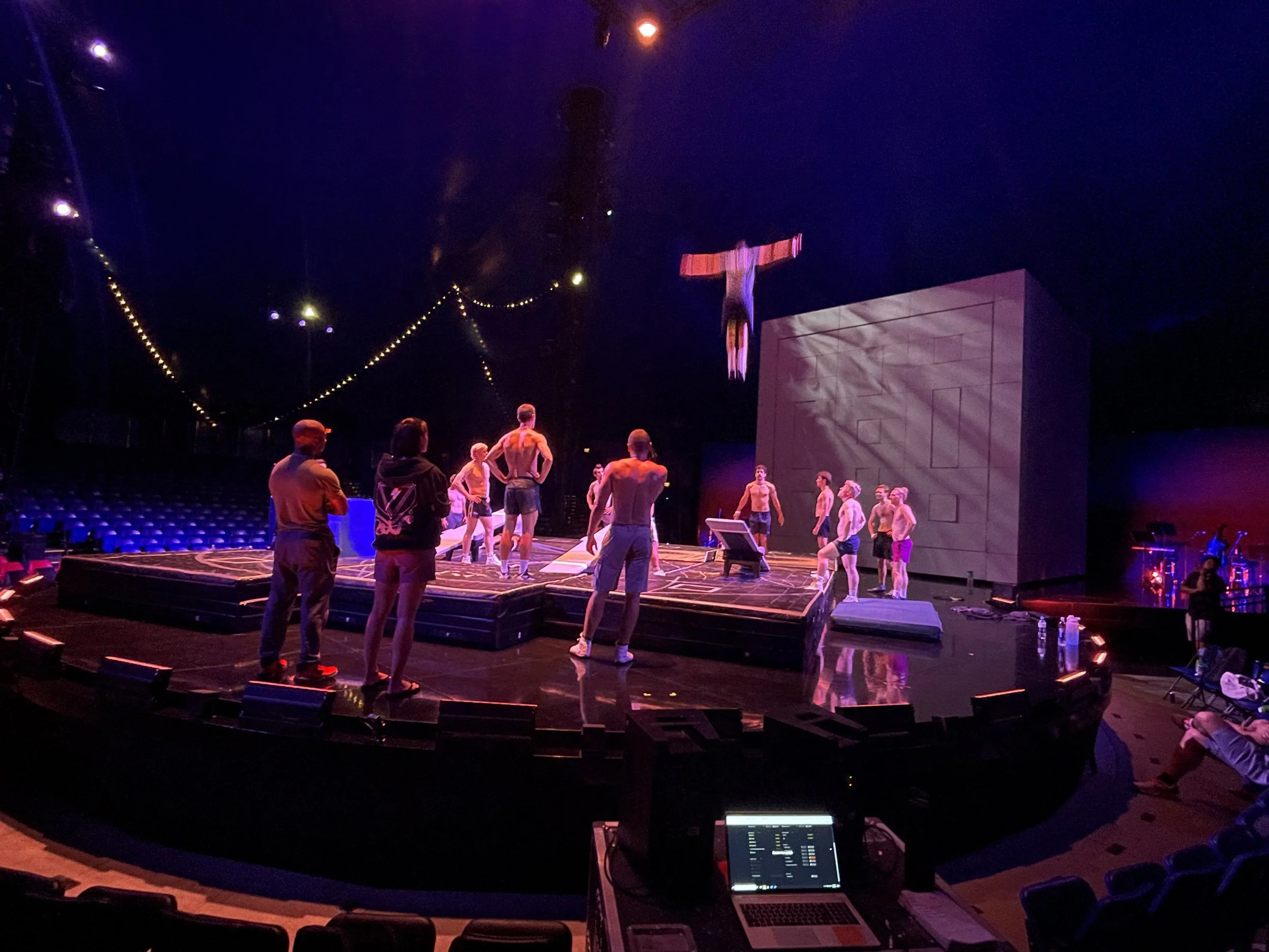 Cirque du Soleil performers rehearsing teeterboard on stage with acrobatic stage equipment in a dimly lit big top setting.