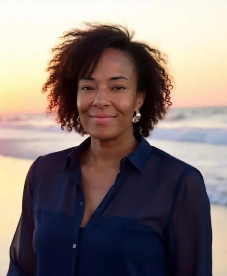 Woman with curly hair smiling at the beach during sunset.