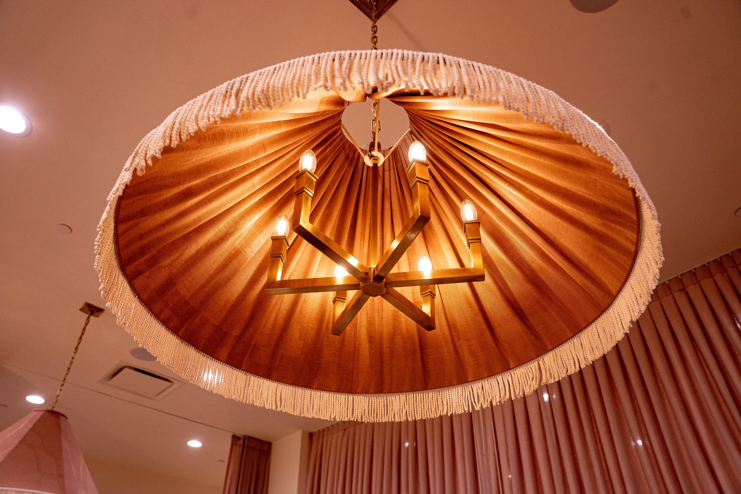 A decorative chandelier with a large, pleated fabric shade and a star-shaped wooden framework with light bulbs, hanging from the ceiling.