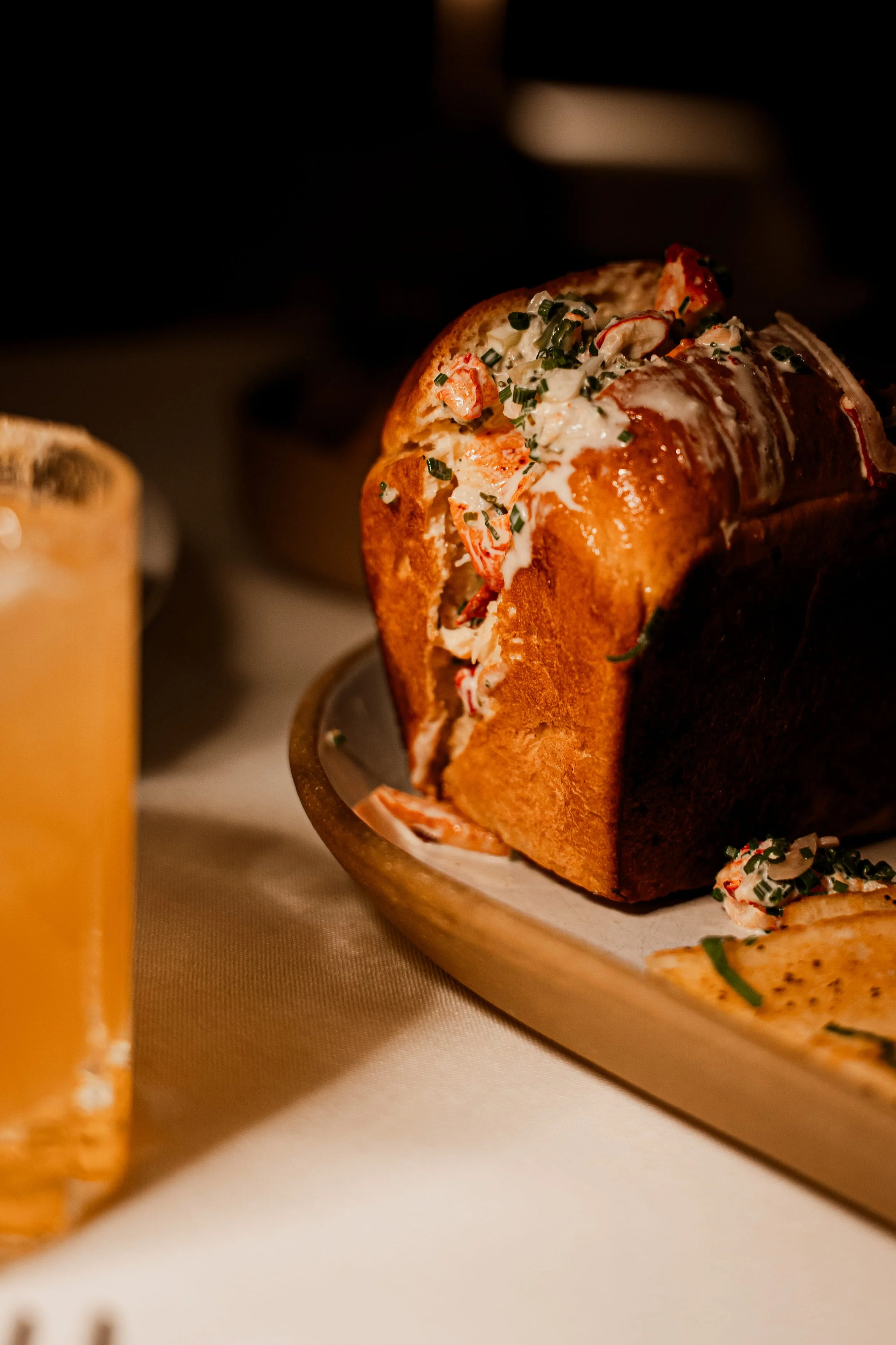 Lobster roll on a wooden platter with lemon wedges in the foreground.