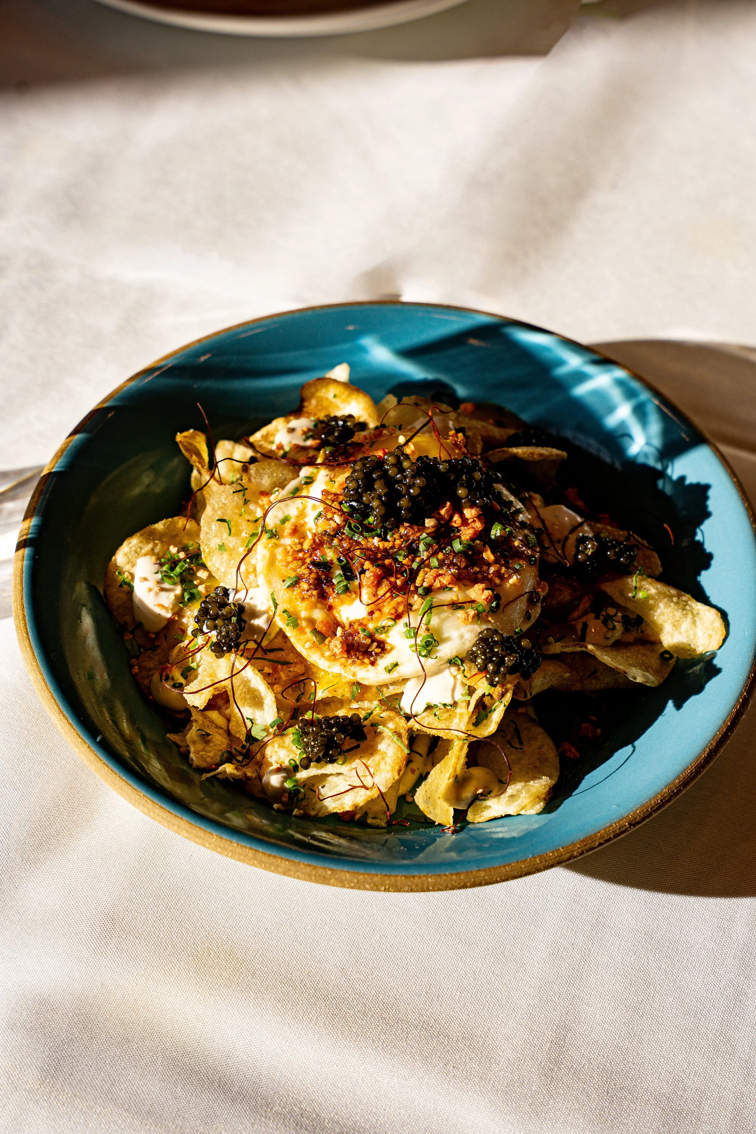 A bowl of loaded chips topped with cheese, sour cream, caviar, chopped chives, and crispy bacon bits.