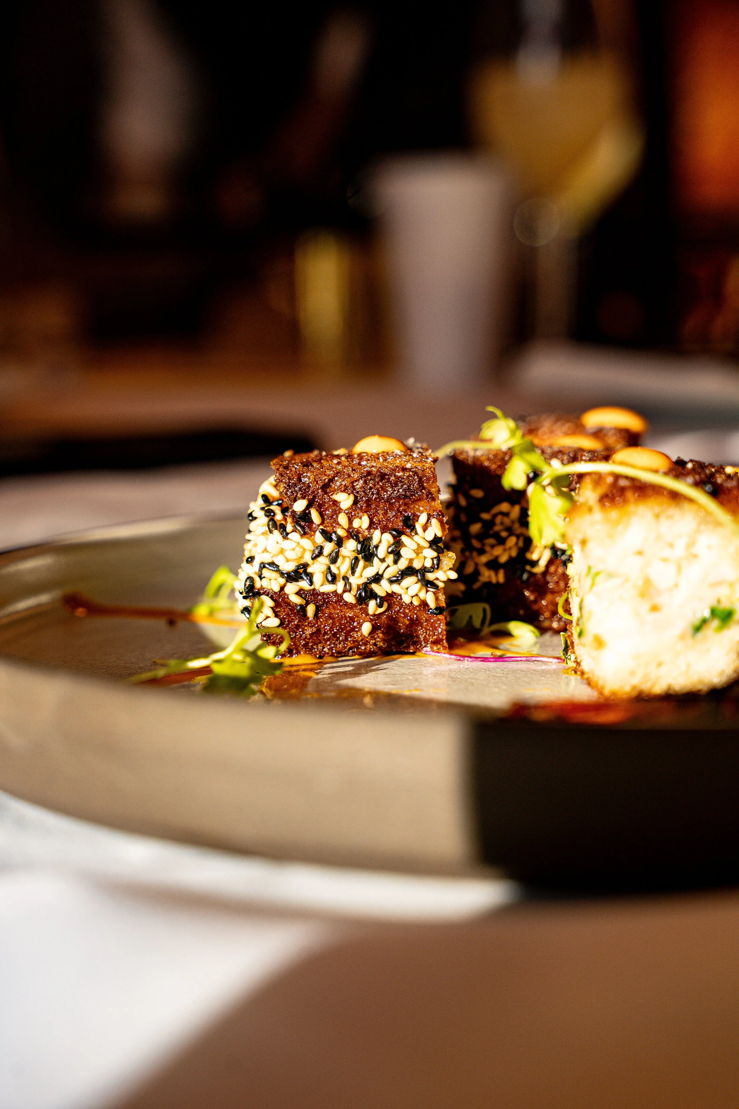 Close-up of a plated appetizer with black and white sesame-seed crusted cubes and greens.