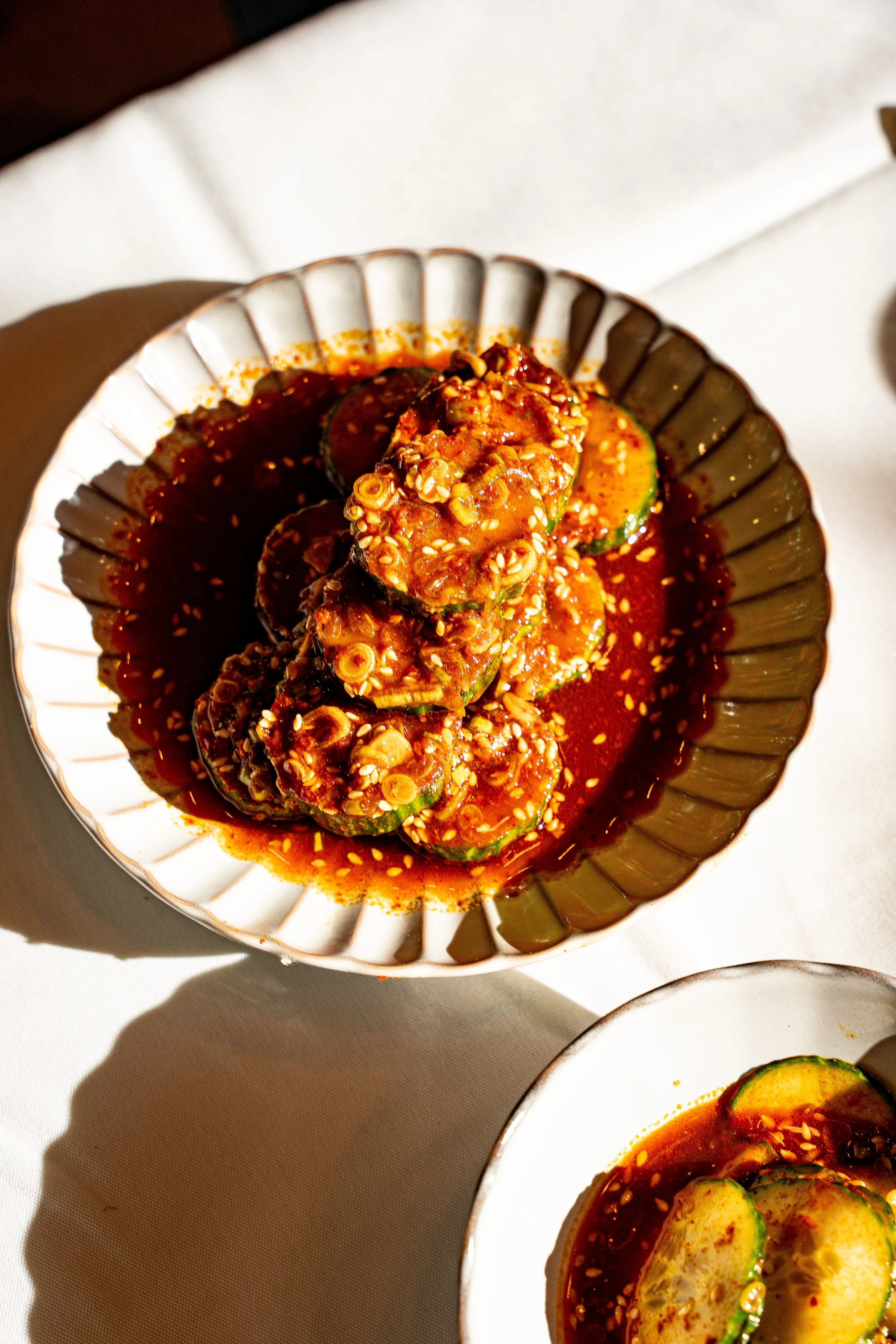 A bowl of cucumber slices topped with a spicy chili sauce and sesame seeds.