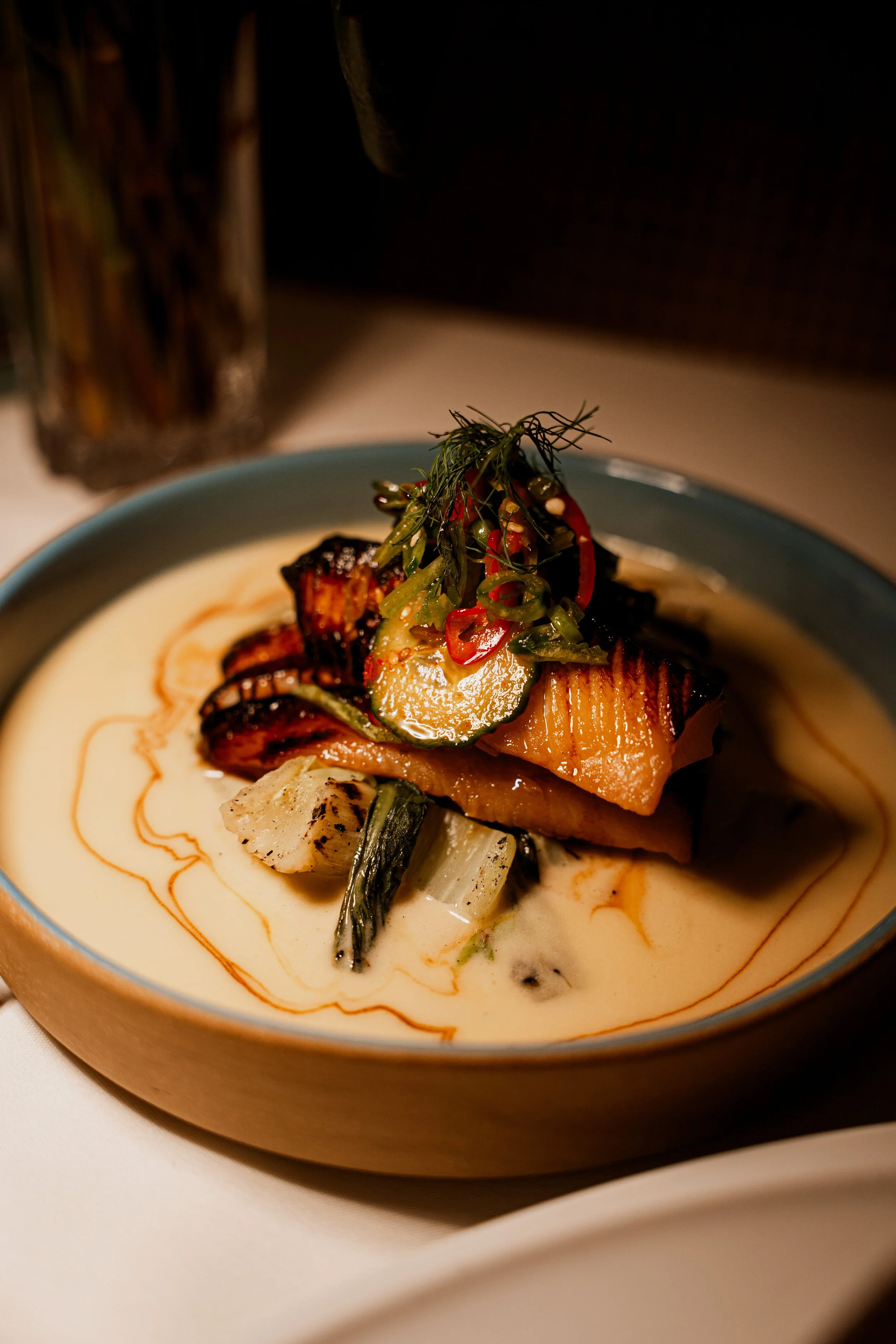 A bowl of seafood and vegetables in creamy sauce, garnished with herbs and sliced chili peppers.