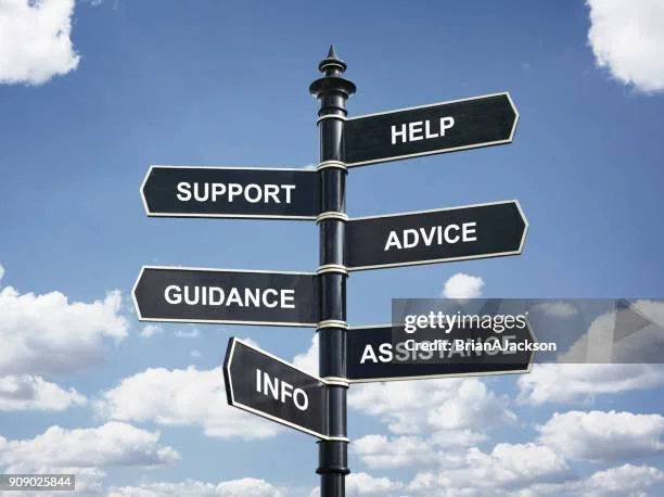 Bir sokak lambası direğinde çeşitli yönleri gösteren talimat levhaları, üzerinde 'Help', 'Support', 'Advice', 'Guidance', 'Assist' ve 'Info' yazıyor.