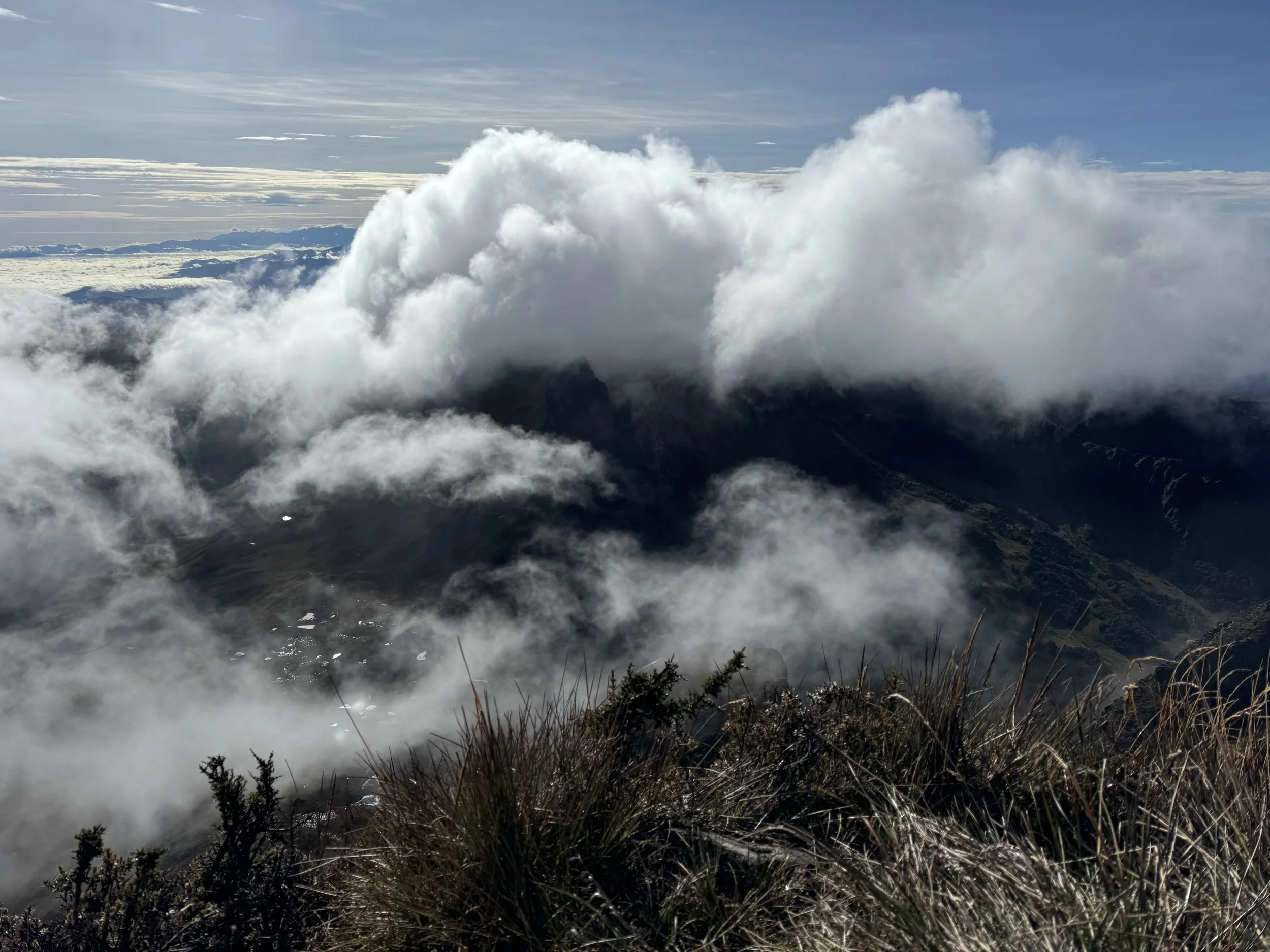 Cloud-covered mountain landscape with grass in the foreground and a sky with thin clouds in the background.