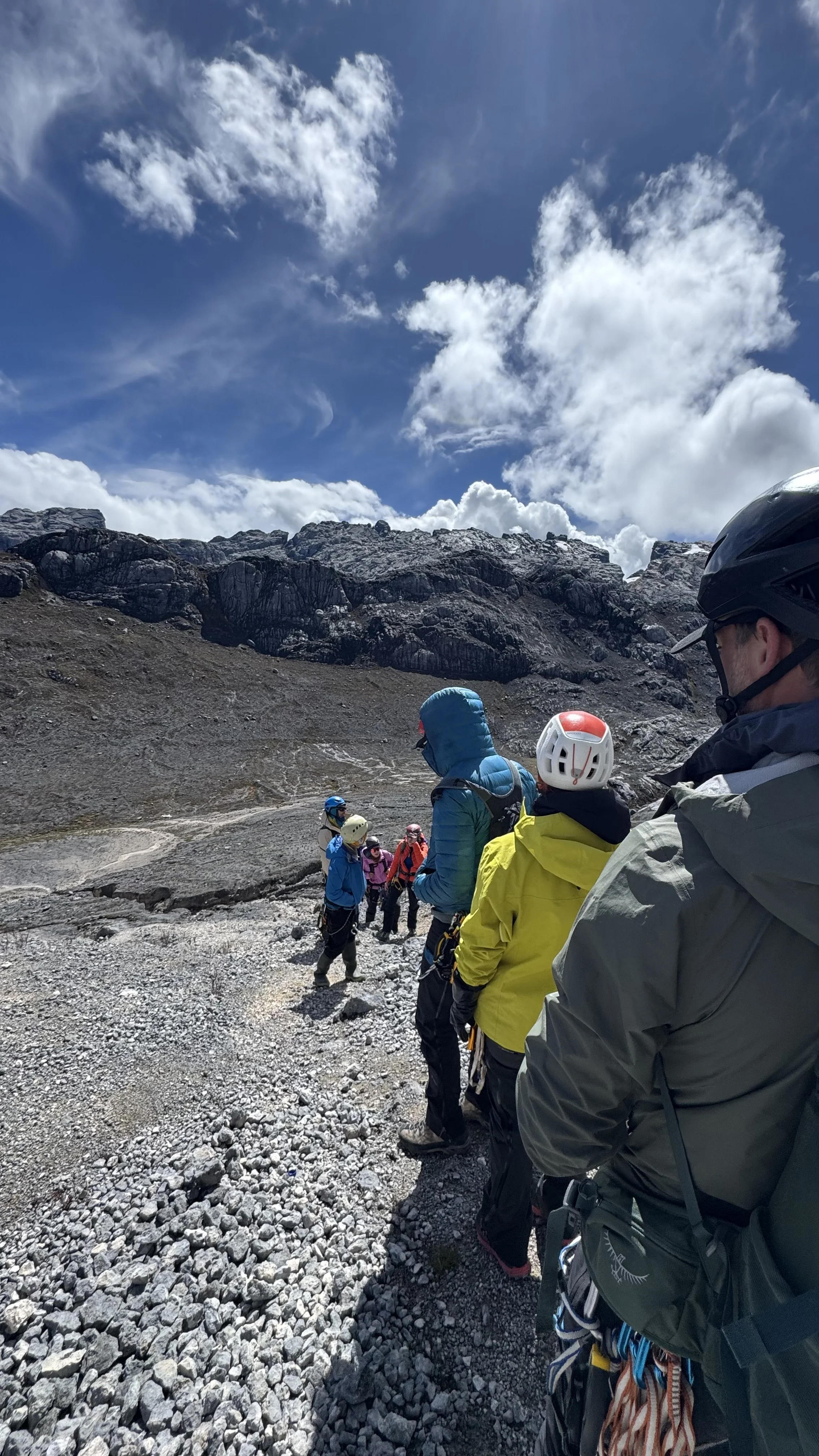 Group of hikers in outdoor gear standing in a rocky mountain landscape with cloudy sky.