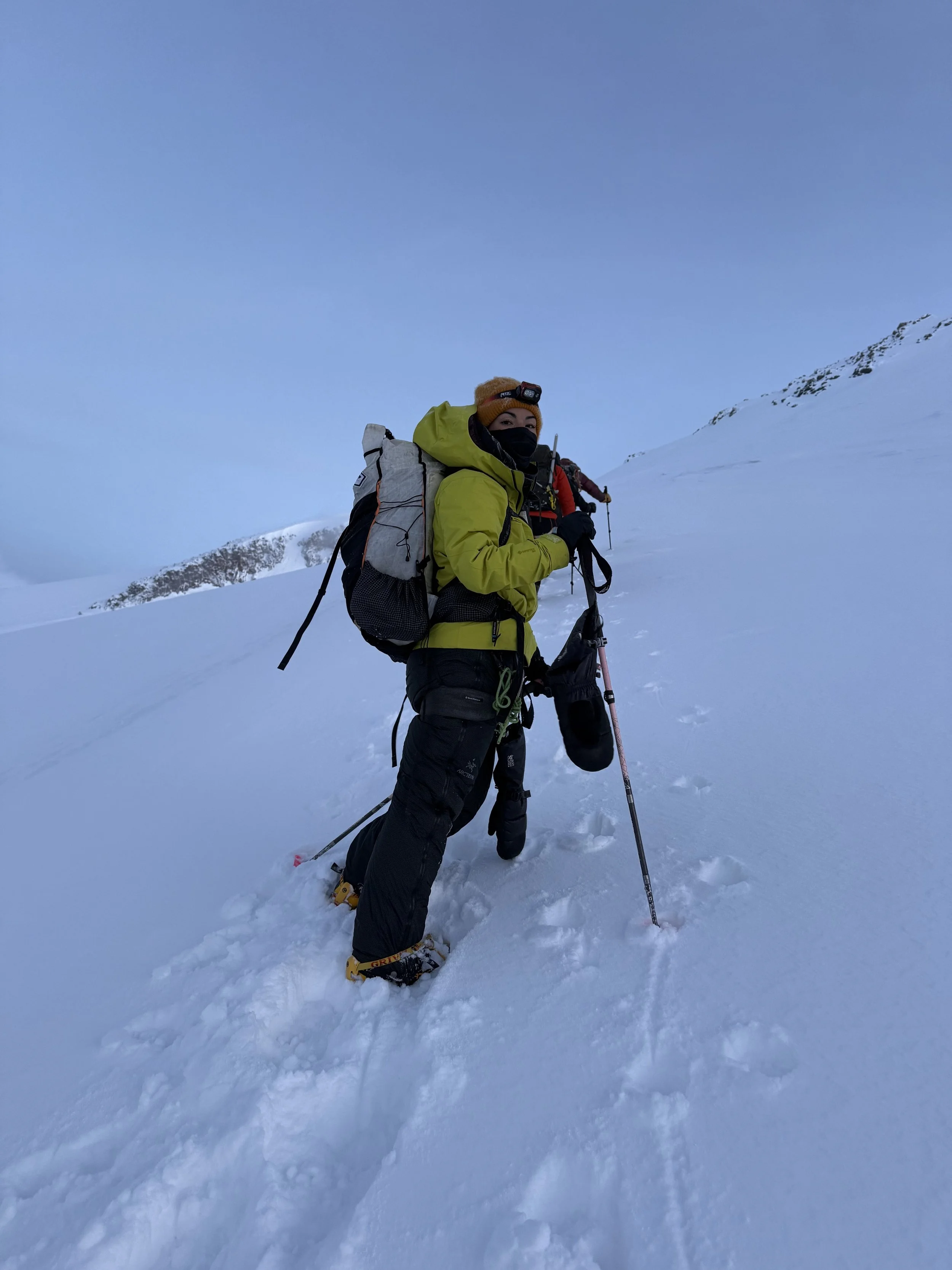 Mountaineer in snow-covered landscape with climbing gear and backpack, snow mountains in the background.