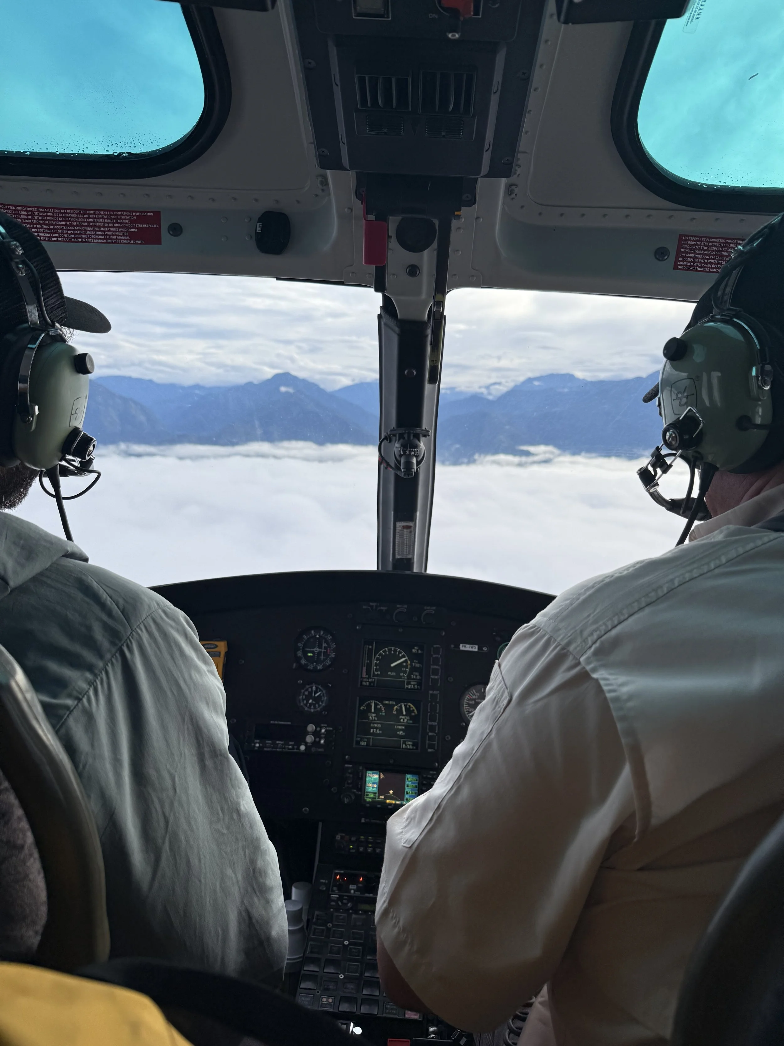 Pilots flying an aircraft above the clouds with mountains in the background.