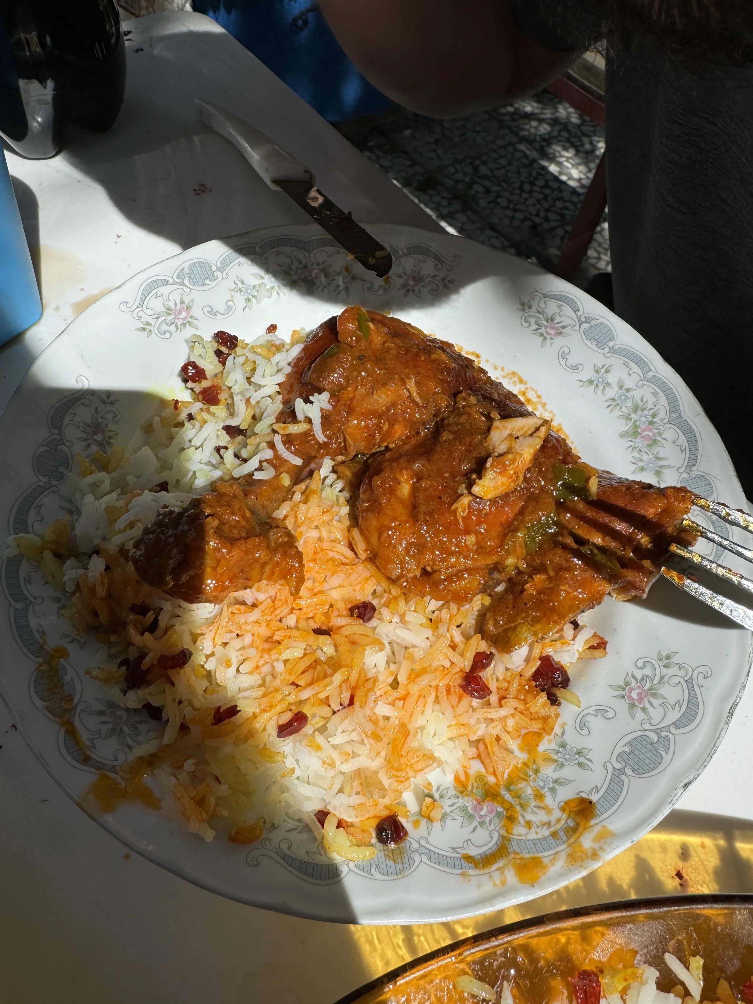 A white plate with a floral pattern containing rice and thick meat curry with vegetables, served with a fork.