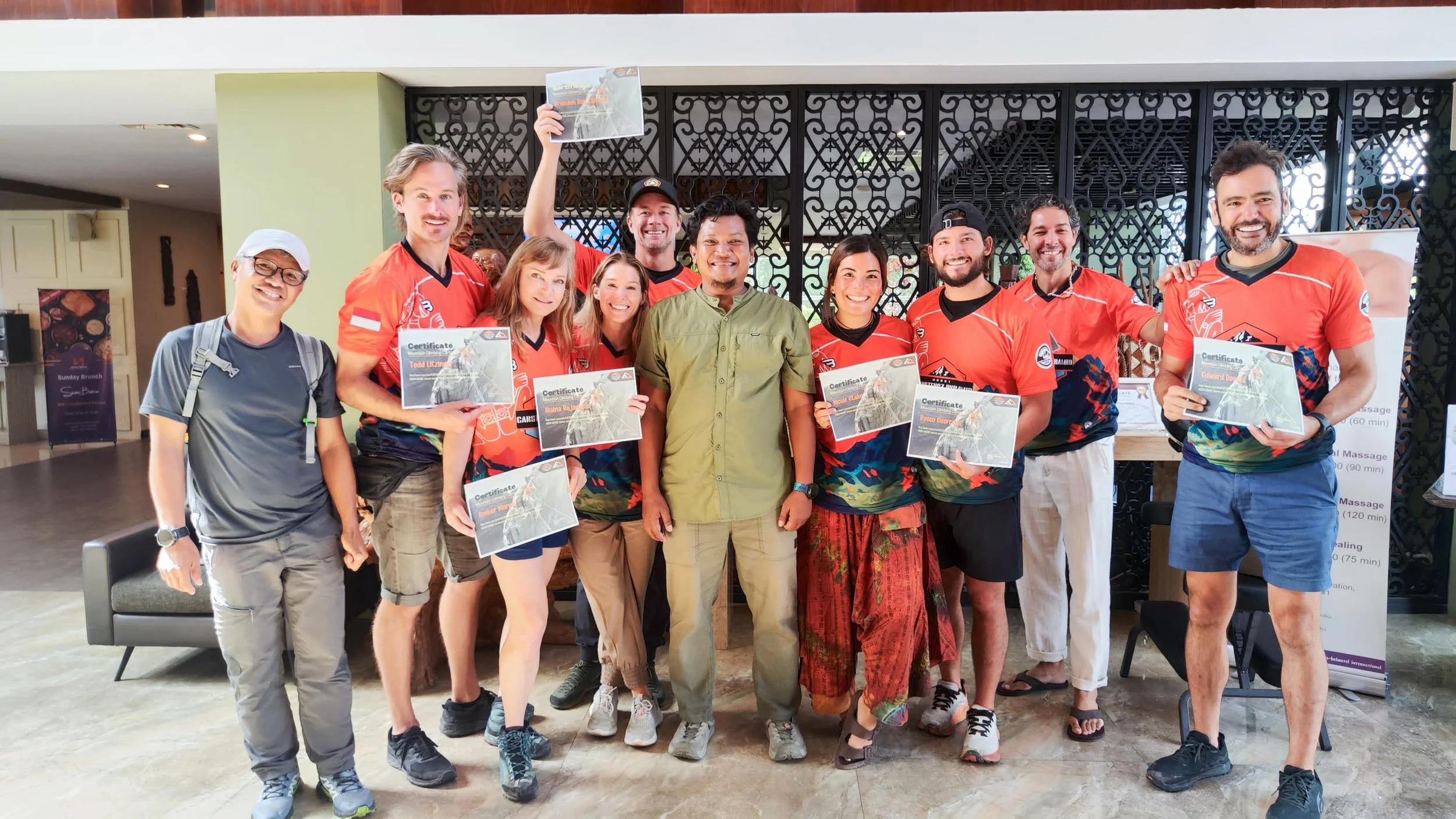 Group of people posing indoors, some holding certificates, some wearing sports jerseys, celebrating an achievement.