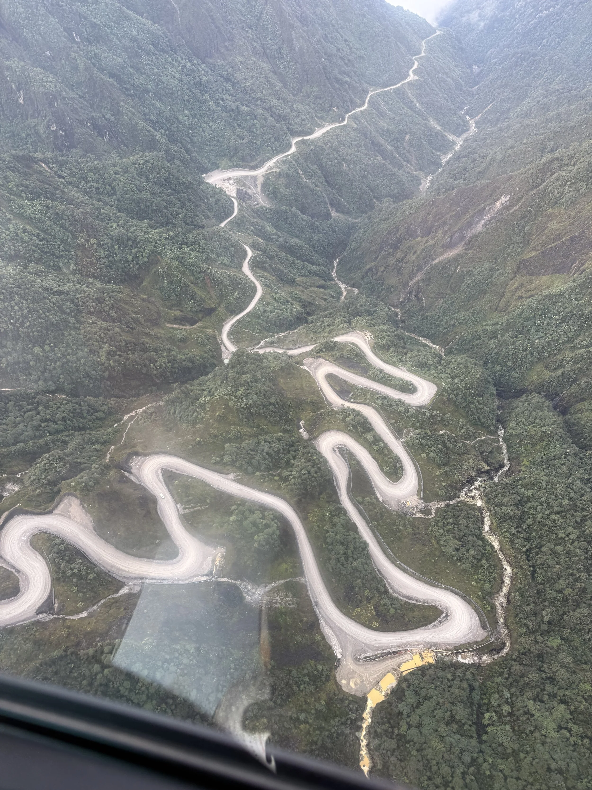 An aerial view of a winding mountain road weaving through lush green forested hills.
