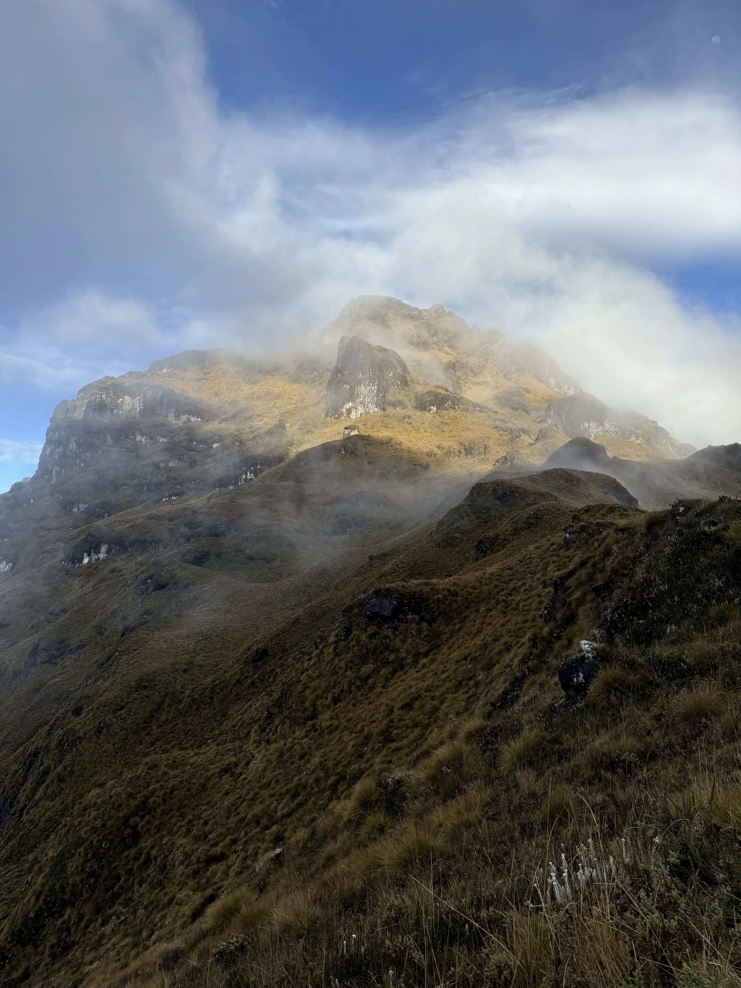 Clouds partially obscure a rugged mountain with grassy slopes in the foreground.