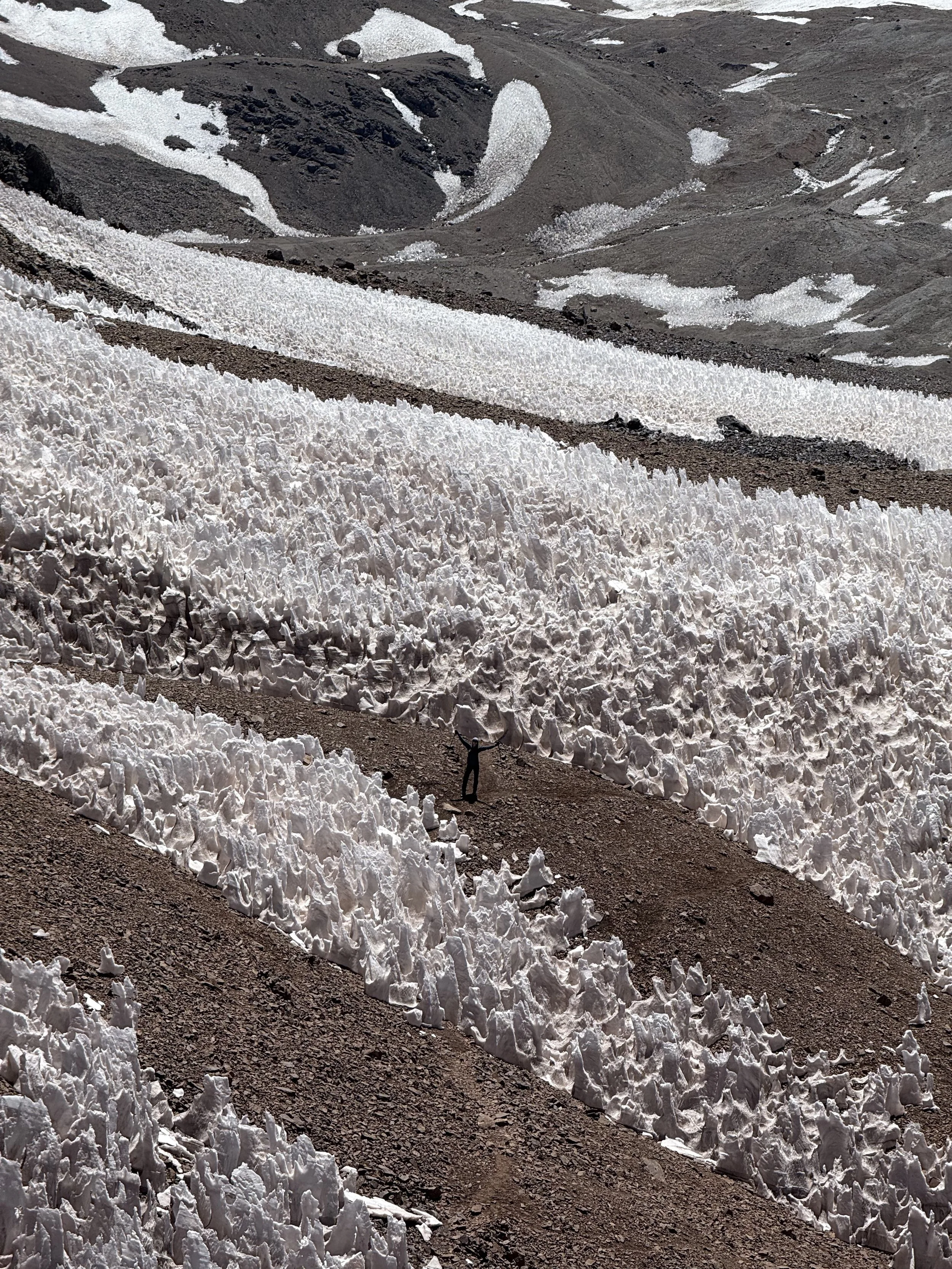 A person standing with arms raised in front of large snow formations in a mountainous landscape.