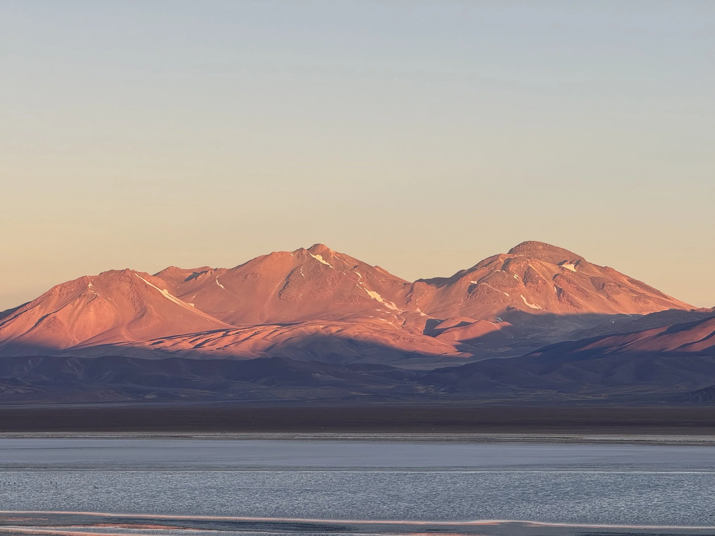 Sunset over a mountain range reflected in a body of water, with a clear sky.