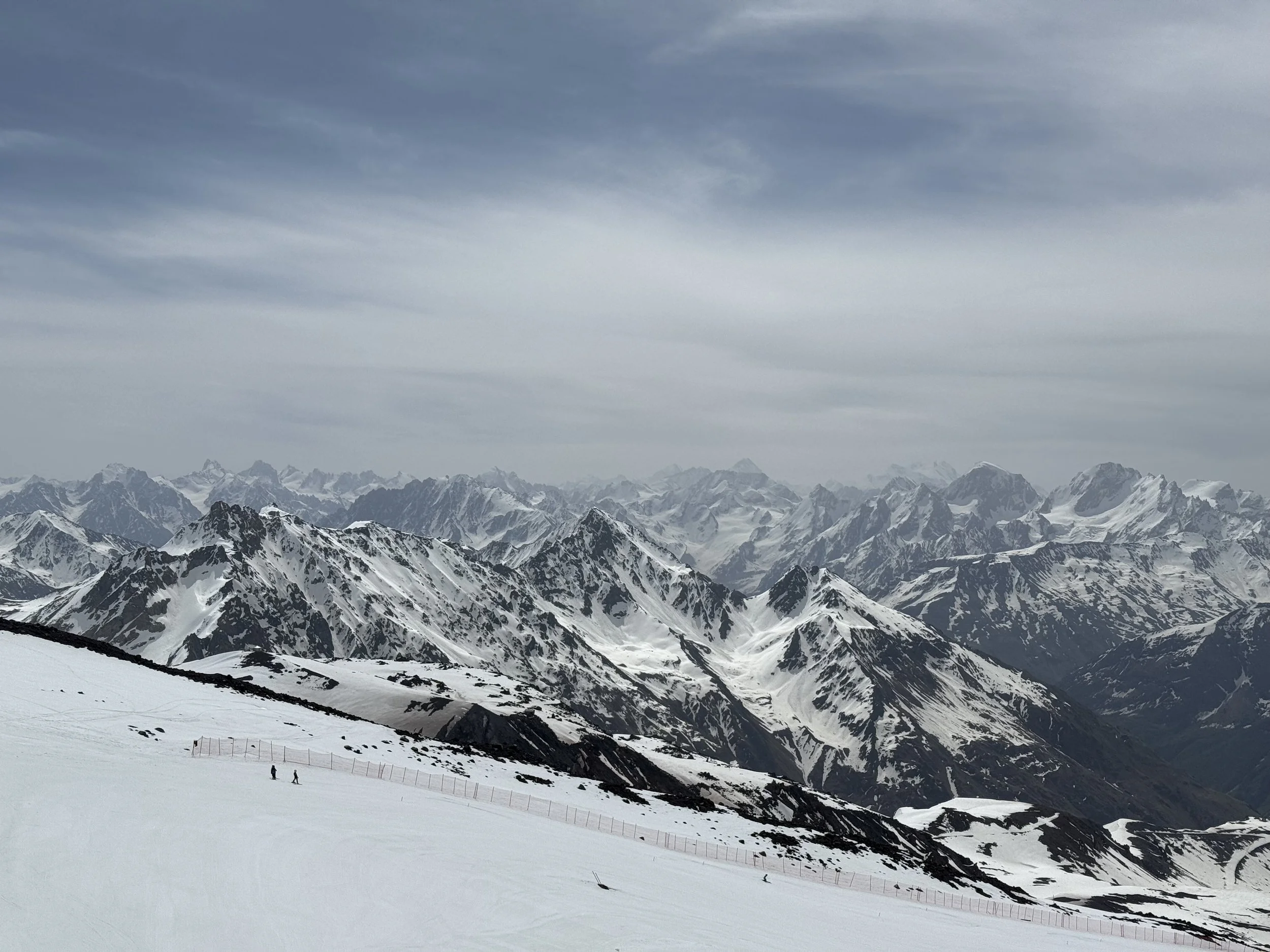 Snow-covered mountain range with dark peaks under a cloudy sky.