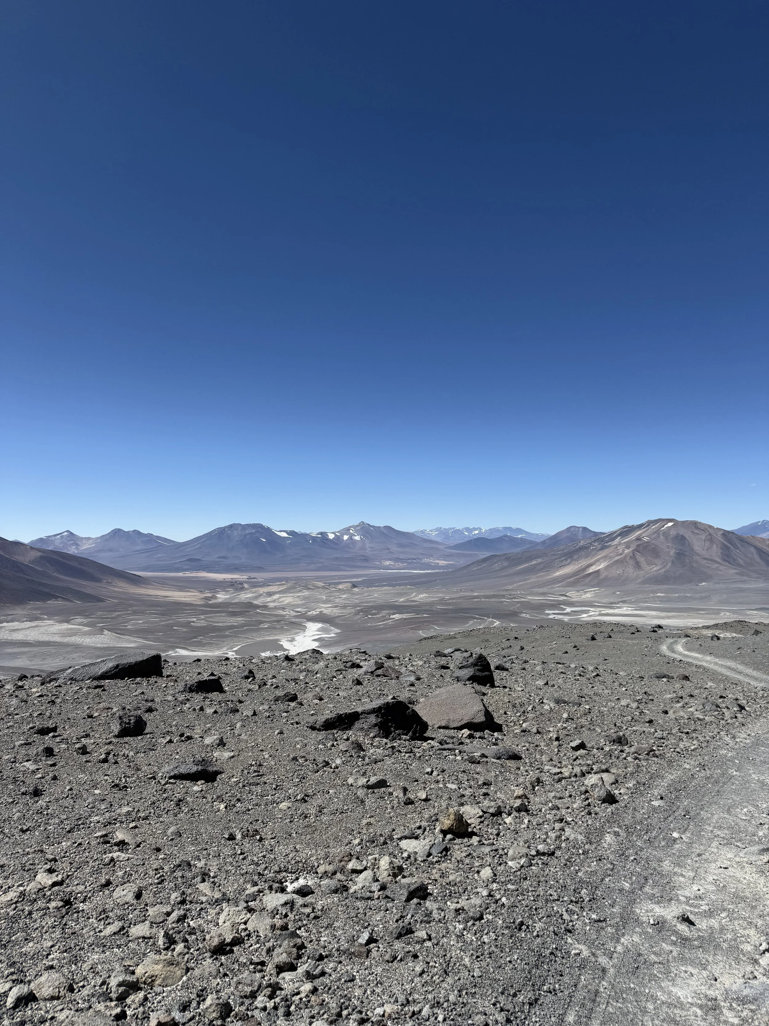 A rugged, rocky desert landscape with mountains in the distance under a clear blue sky.