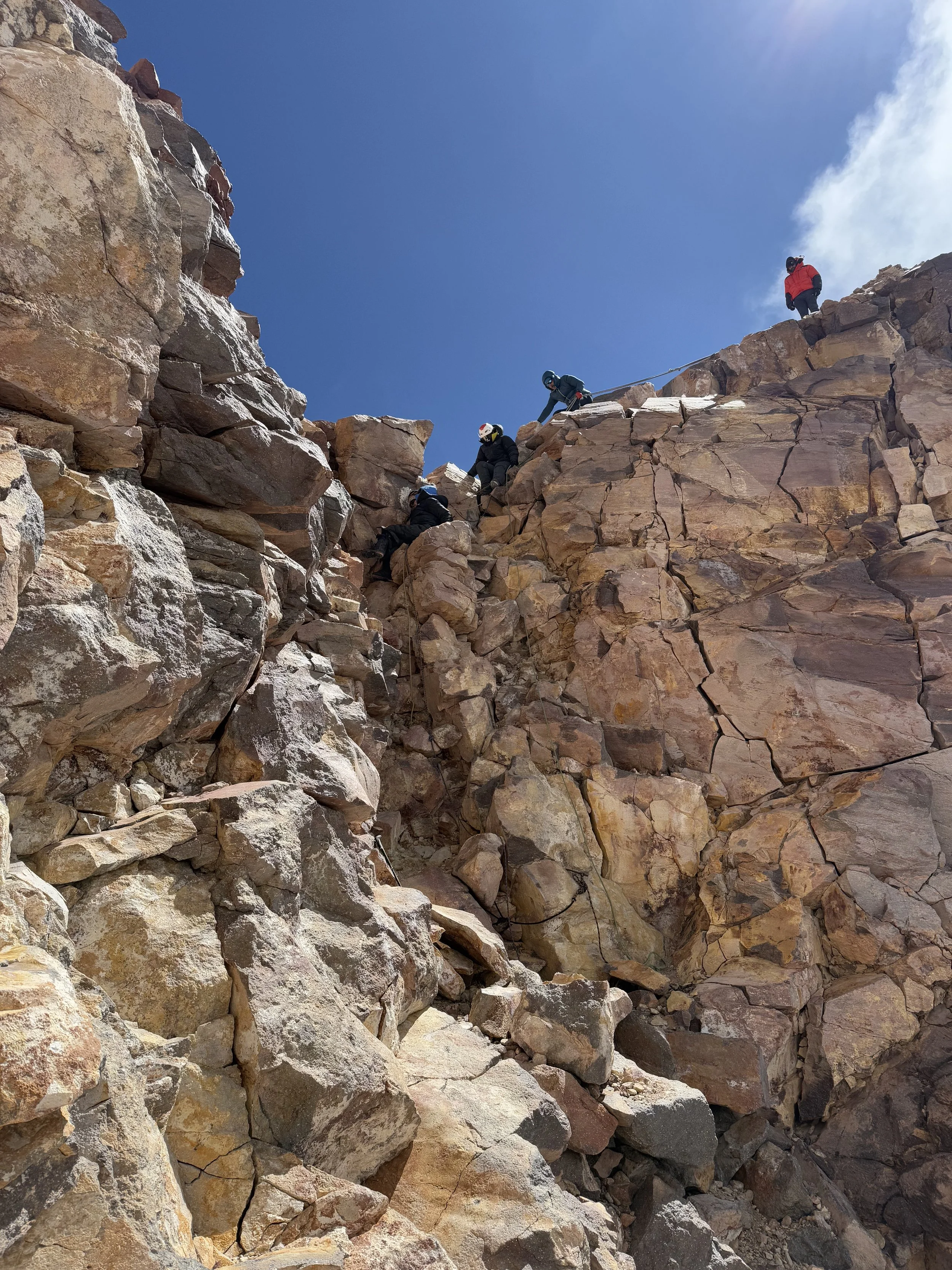 Five climbers ascending a rocky mountain face under a clear blue sky.