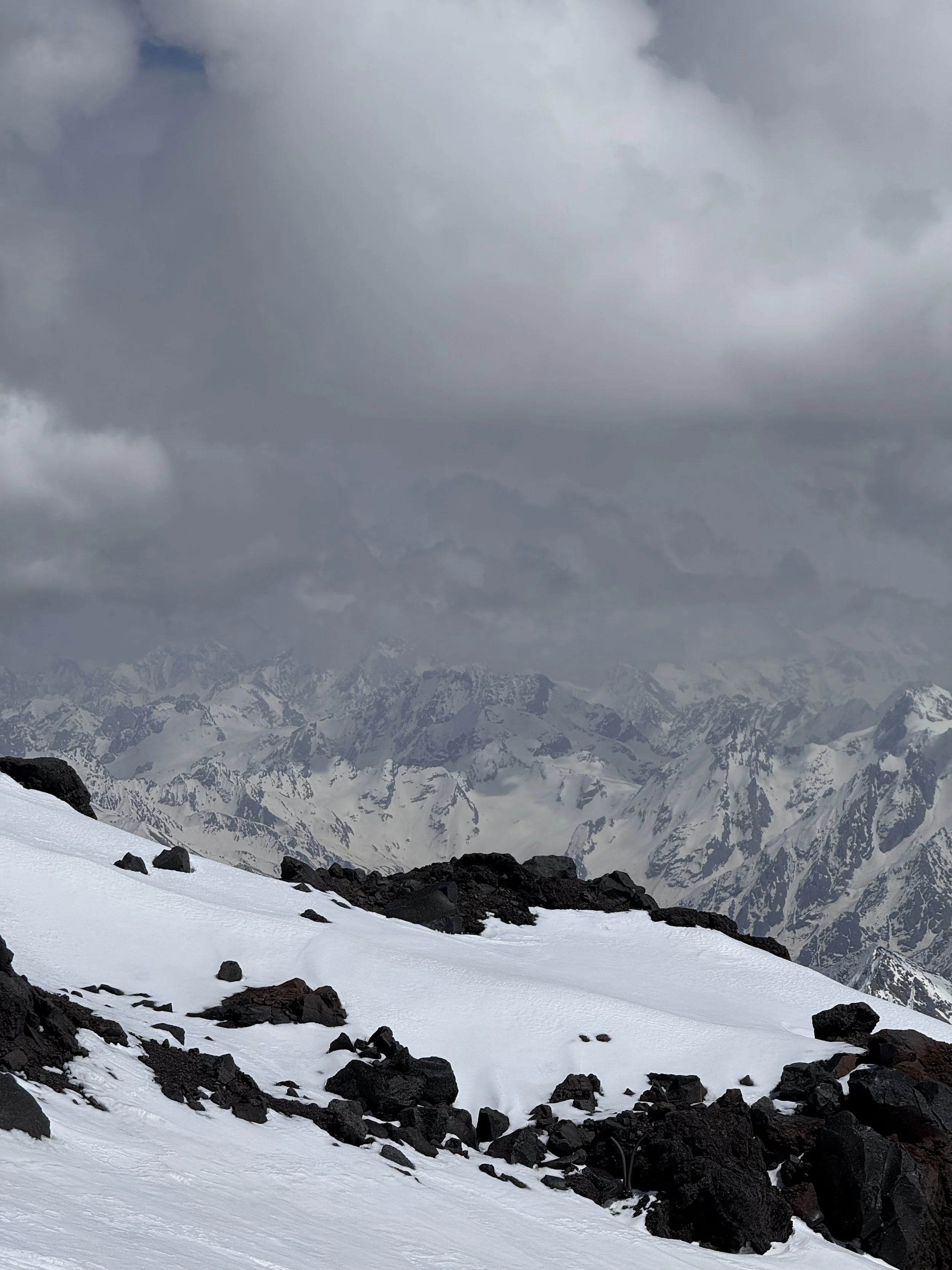 Snow-covered mountain landscape with dark rocks and a cloudy sky.